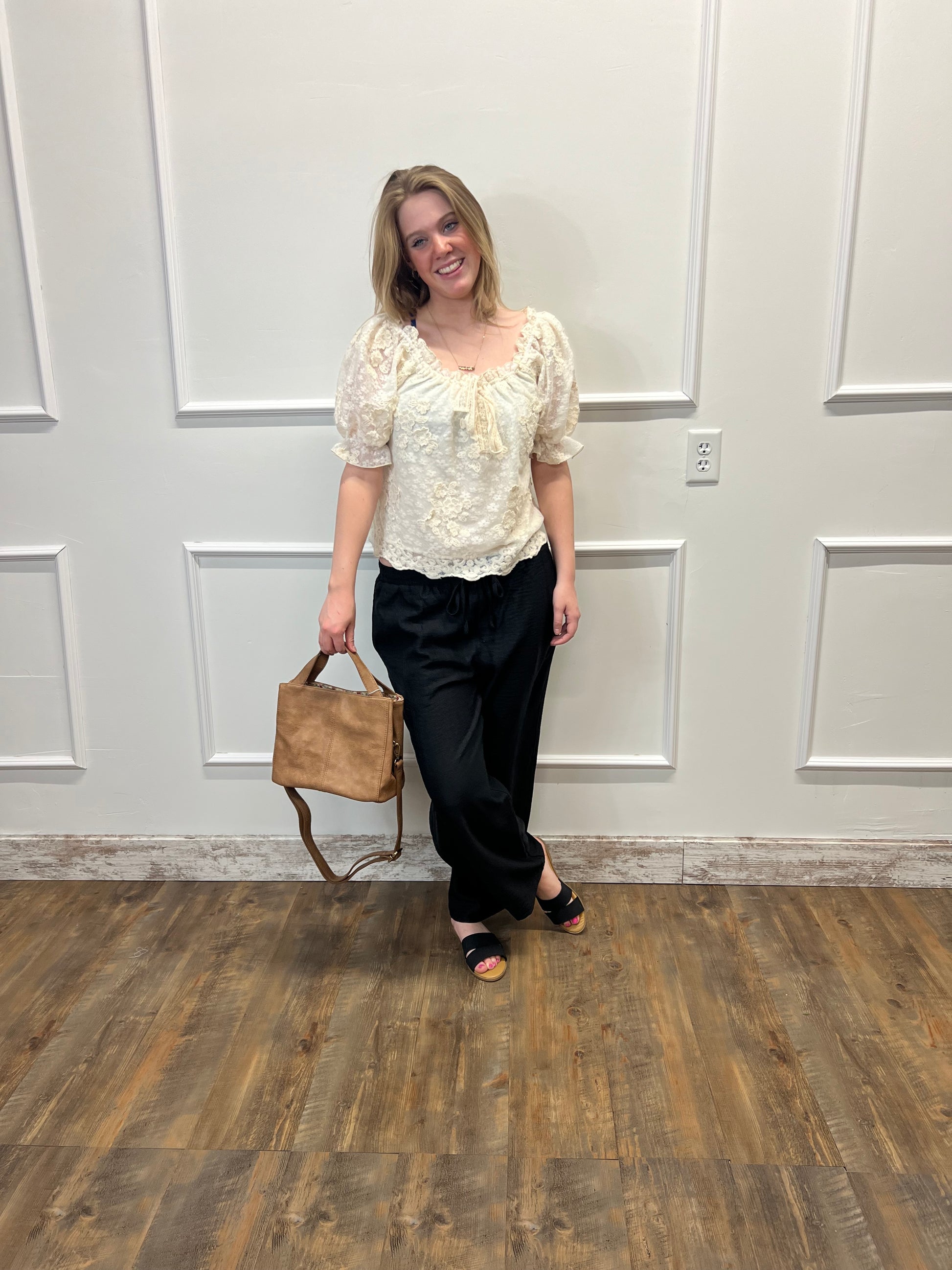 Woman holding a brown handbag in front of a white door on a wooden floor.