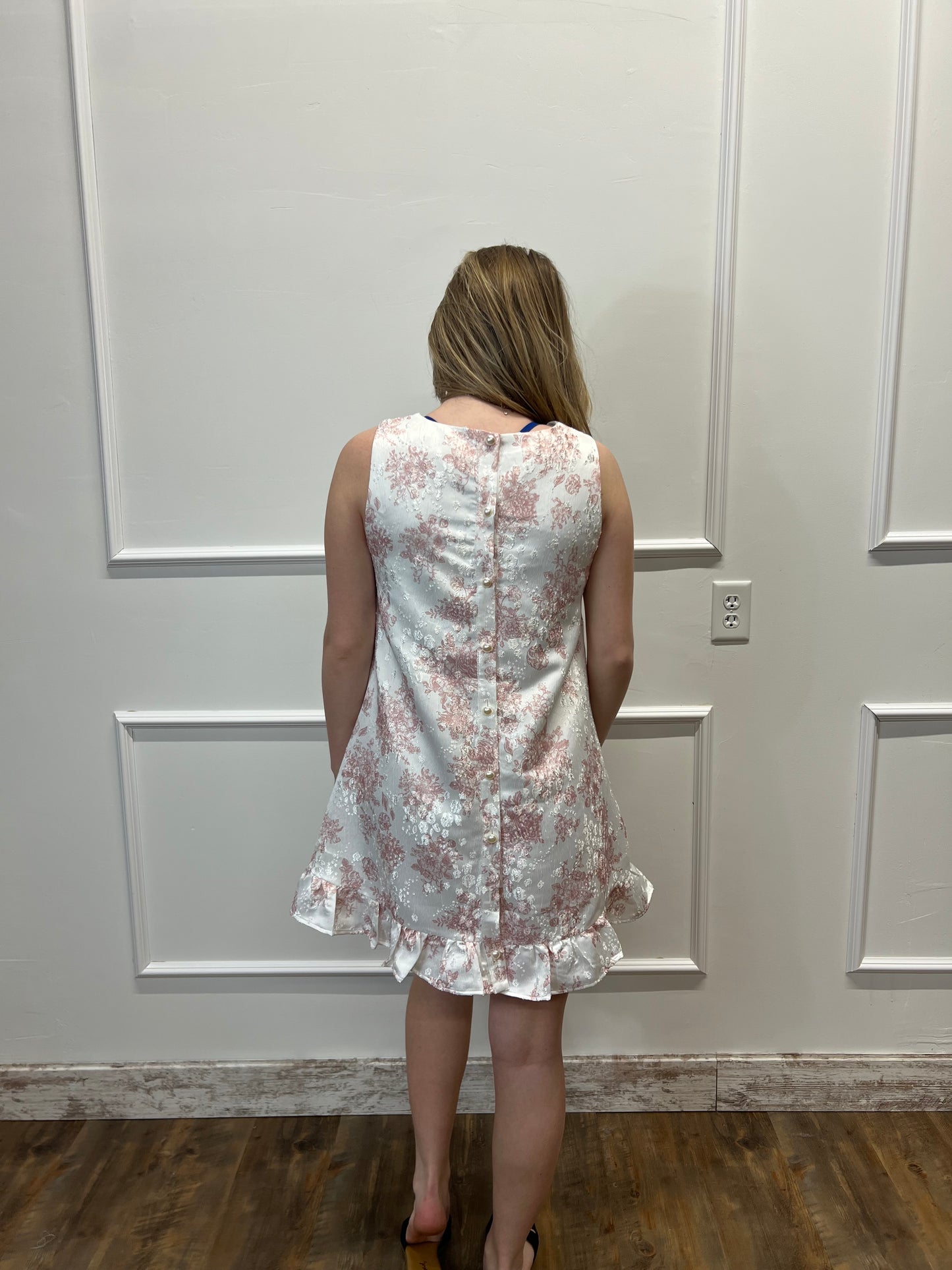 Person wearing a floral dress standing against a white paneled wall.
