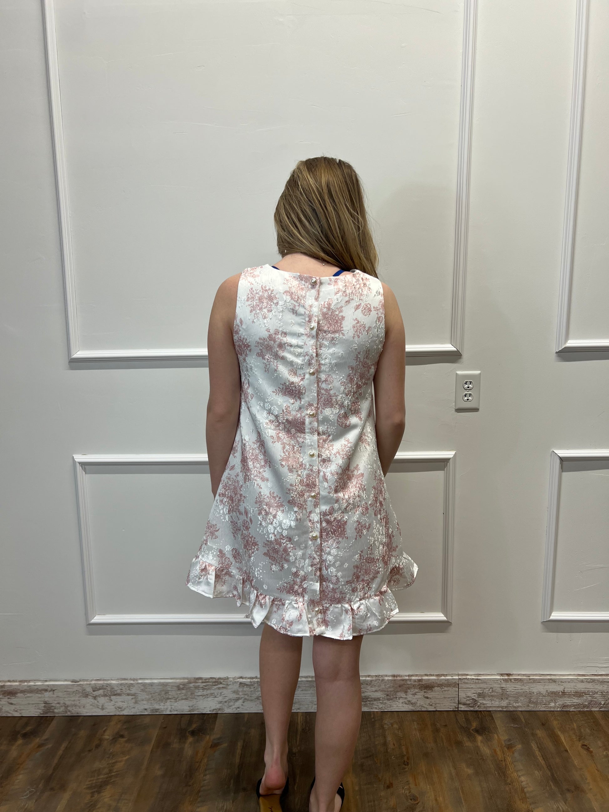 Person wearing a floral dress standing against a white paneled wall.