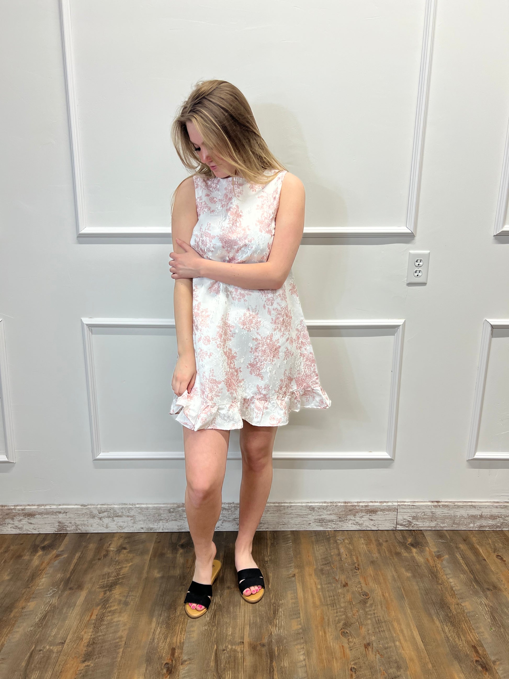 Person wearing a floral dress standing in front of a white door.