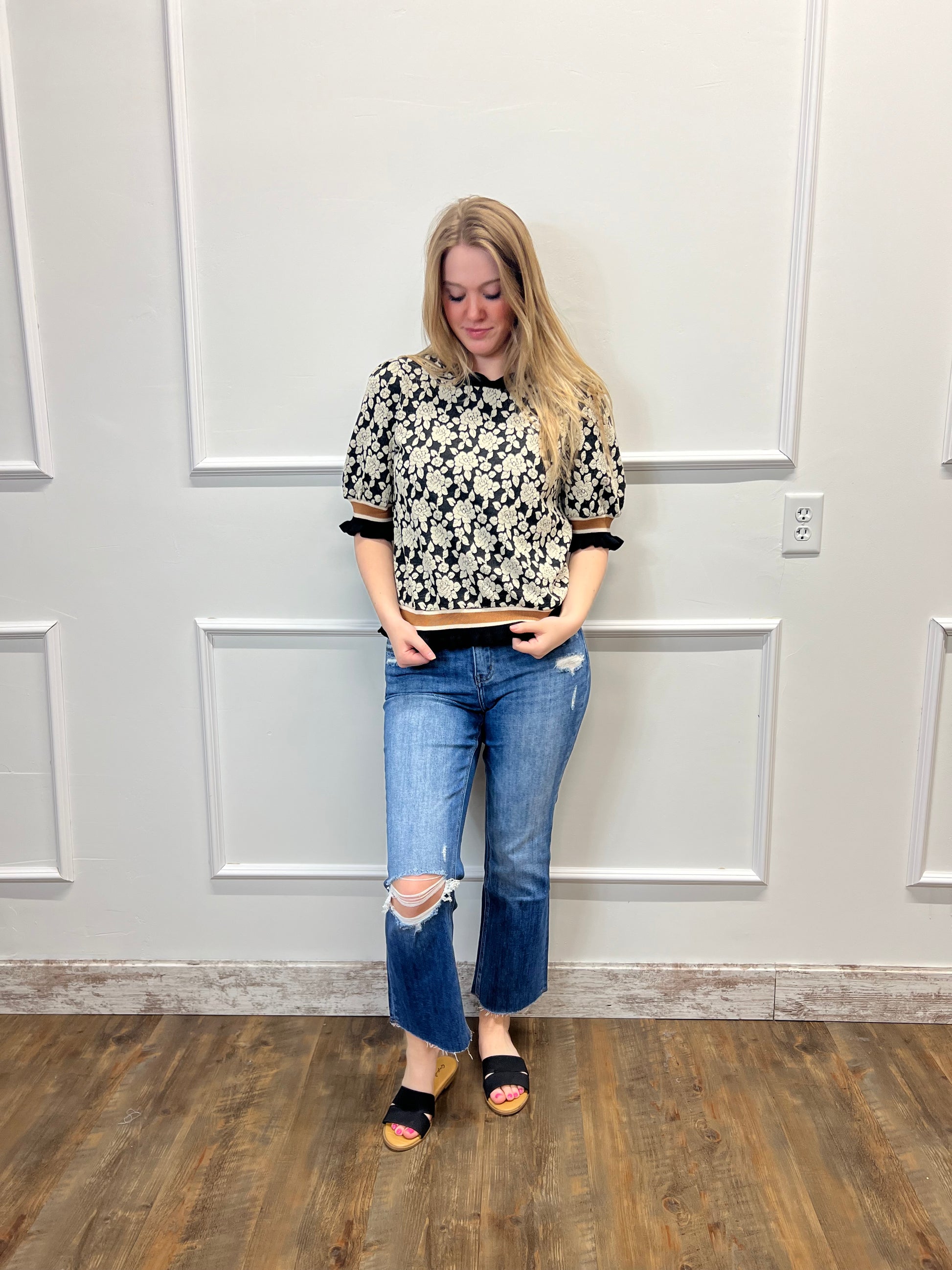 Woman standing in a room with wooden flooring and white walls.