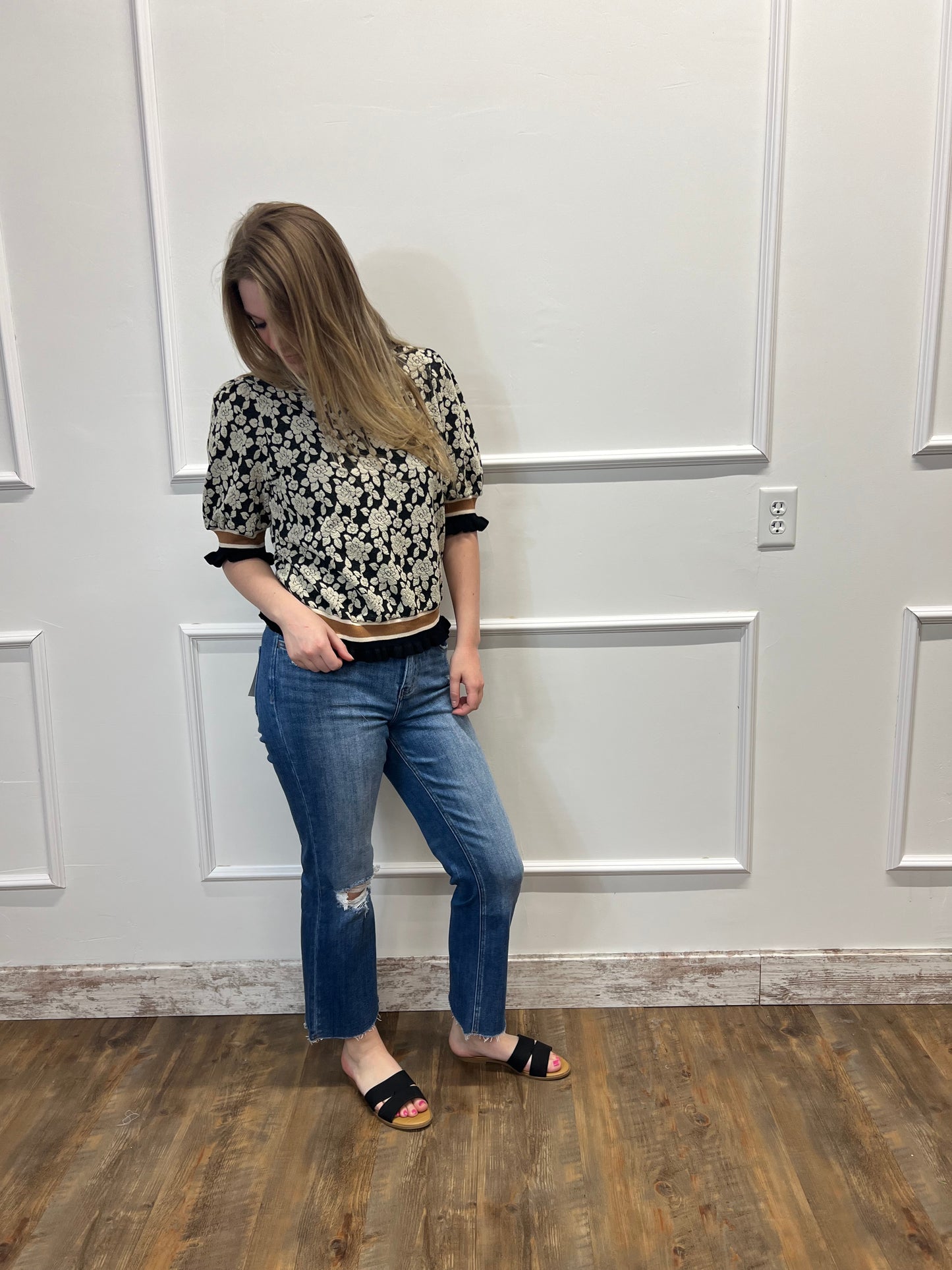 Person wearing a patterned shirt and jeans standing in front of a white door.