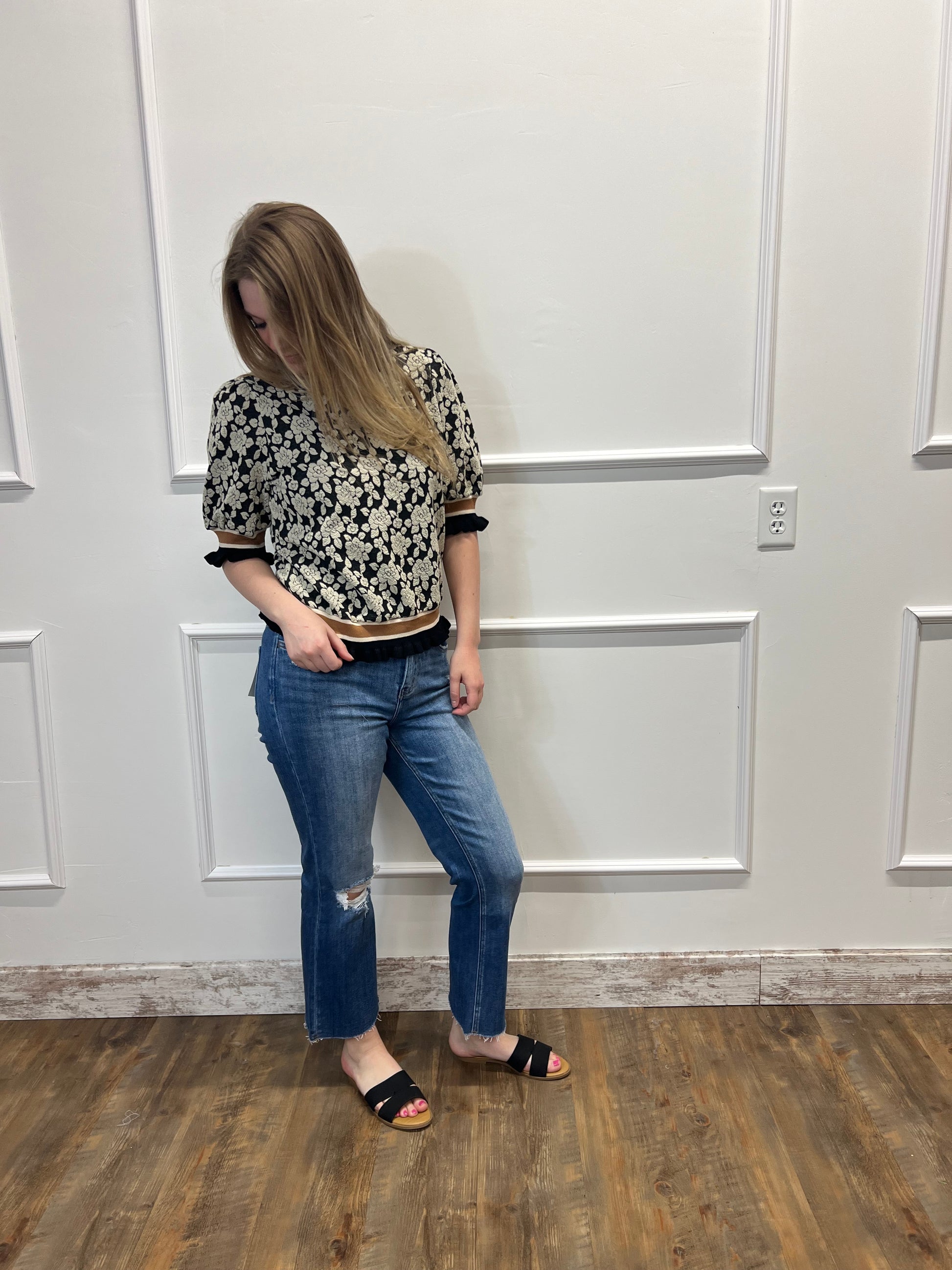 Person wearing a patterned shirt and jeans standing in front of a white door.