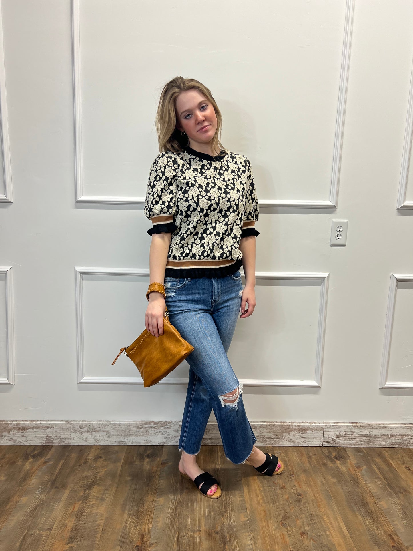 Woman standing in front of a white door holding a brown clutch.