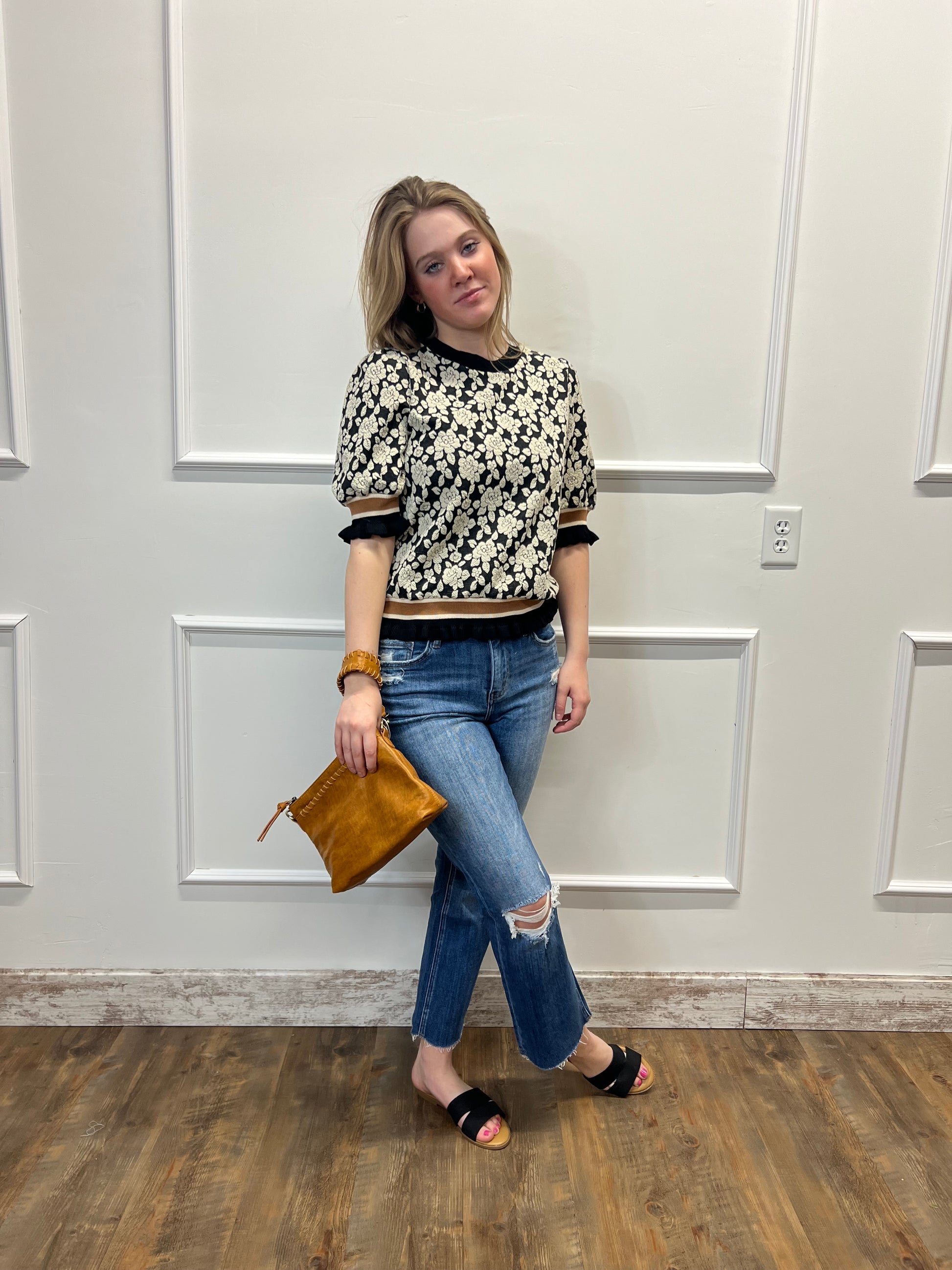 Woman standing in front of a white door holding a brown clutch.