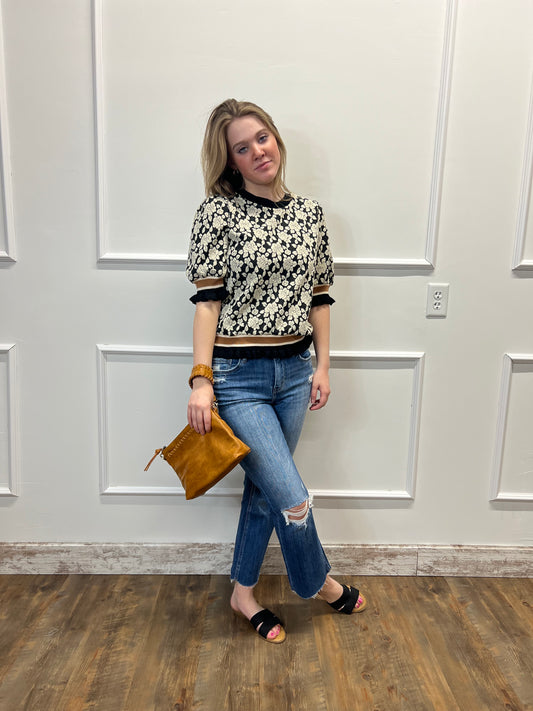 Woman standing in front of a white door holding a brown clutch.
