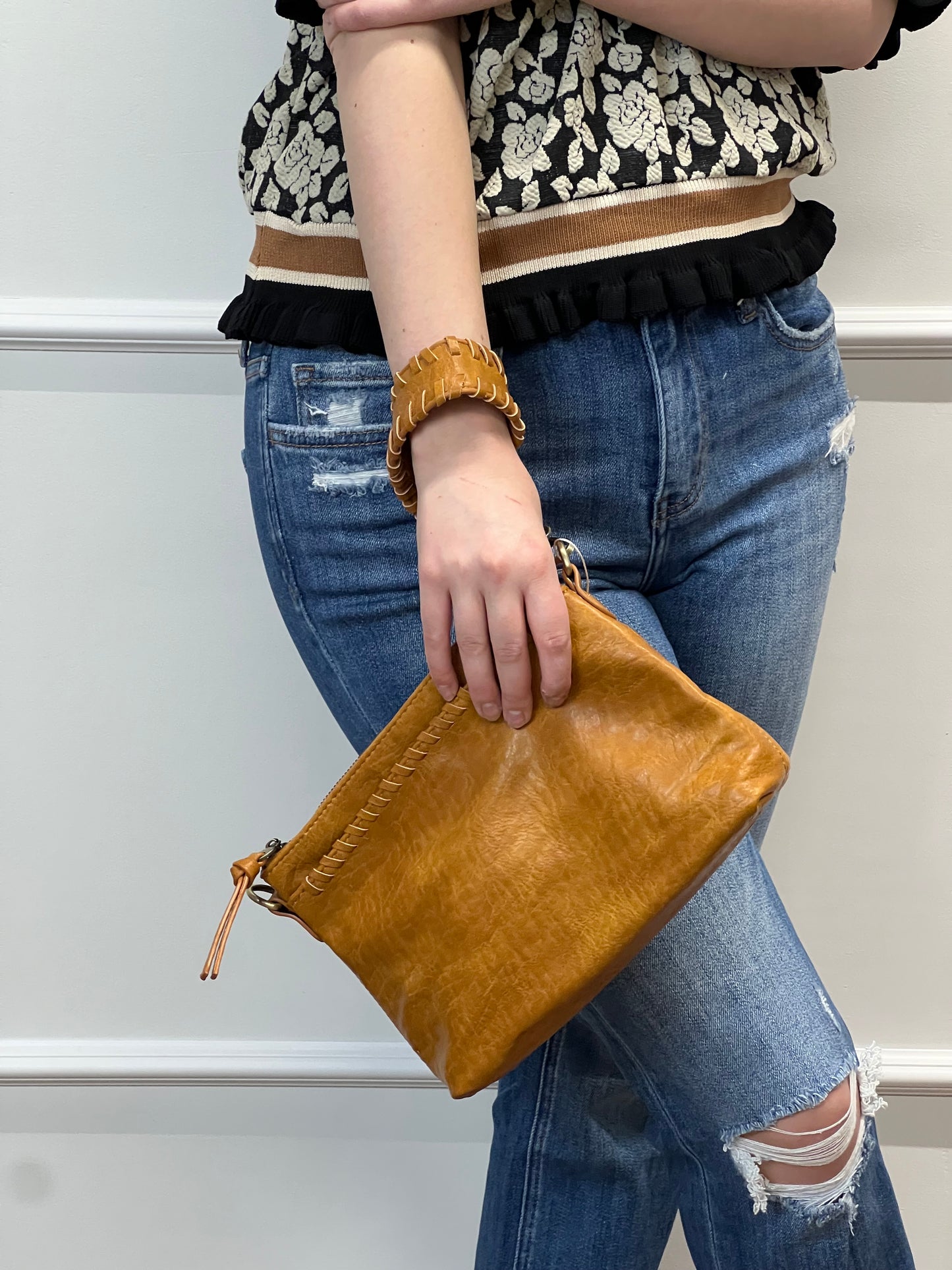 Person holding a brown leather clutch bag with a neutral background