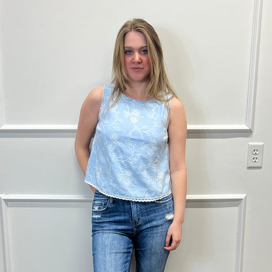 Person wearing a light blue top and jeans standing in front of a white paneled wall.