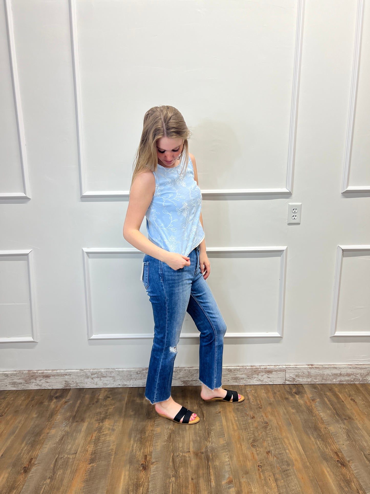 Person wearing a light blue top and jeans standing in front of a white door.
