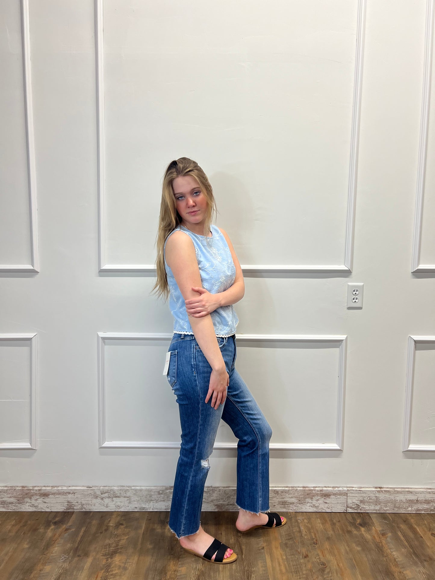Person wearing a light blue top and jeans standing in front of a white door.