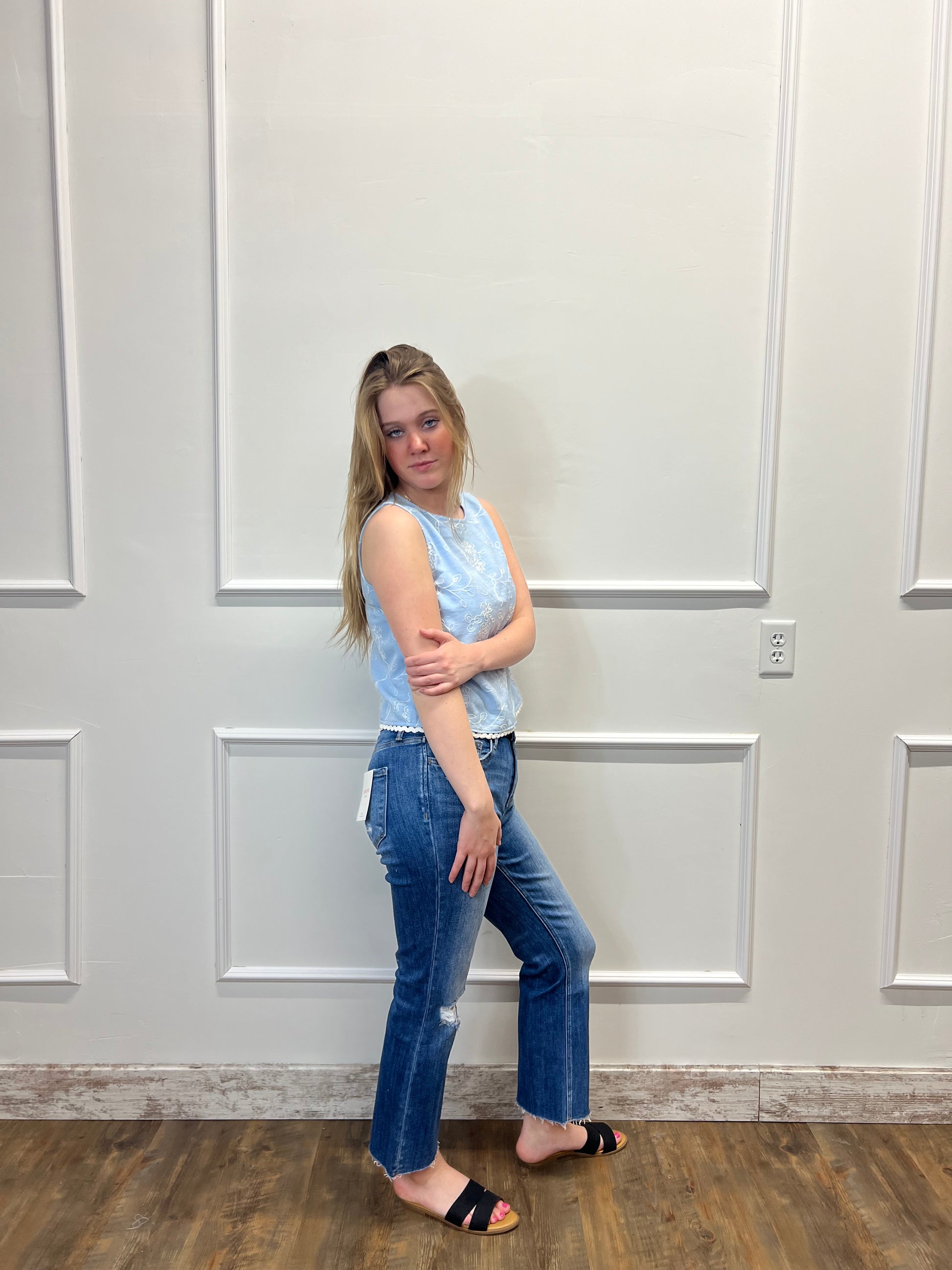 Person wearing a light blue top and jeans standing in front of a white door.