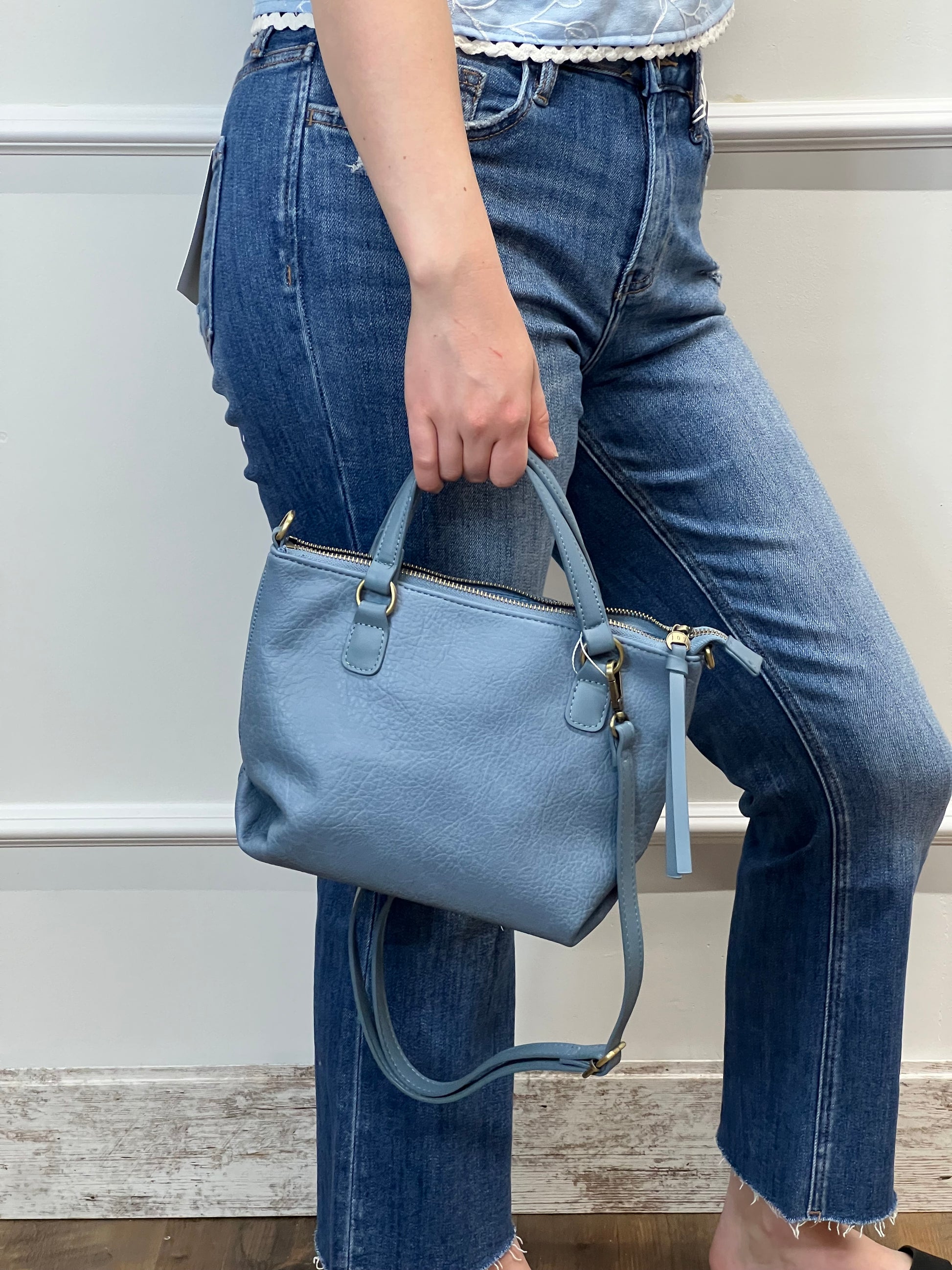 Person holding a blue backpack with jeans in the background