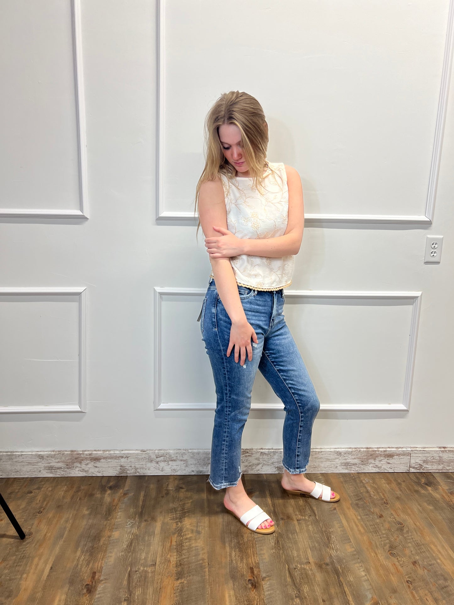 Person in a white shirt and blue jeans standing on a wooden floor with a white wall.