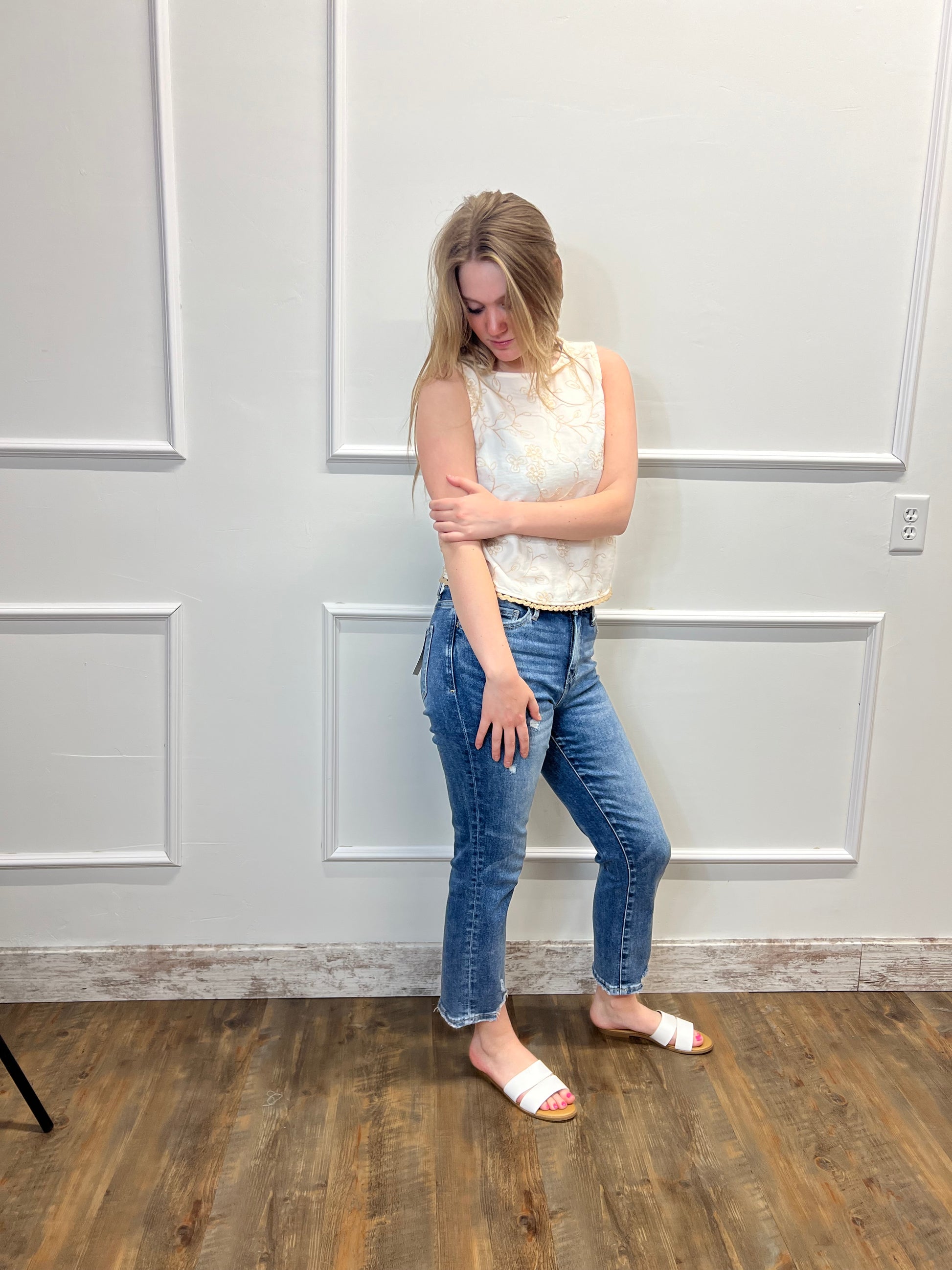 Person in a white shirt and blue jeans standing on a wooden floor with a white wall.