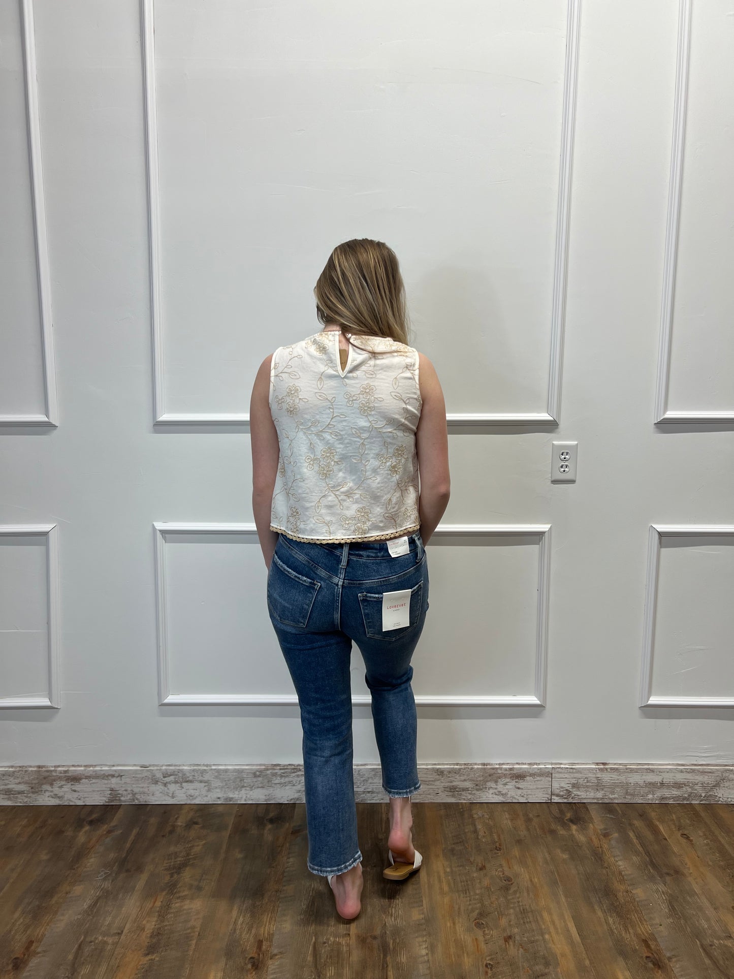 Person wearing a patterned shirt and jeans standing in front of a white door.