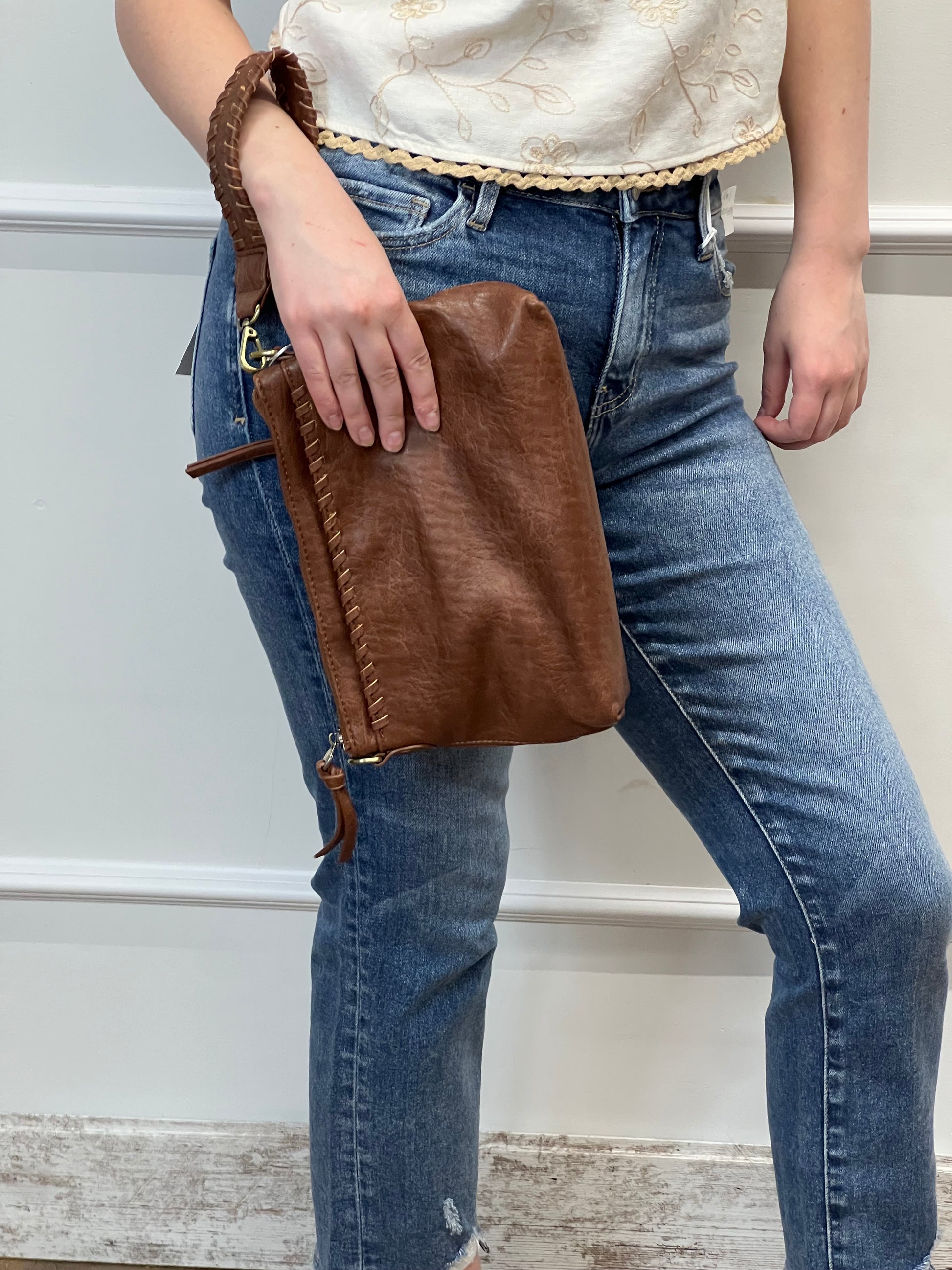 Person holding a brown leather clutch bag with a neutral background