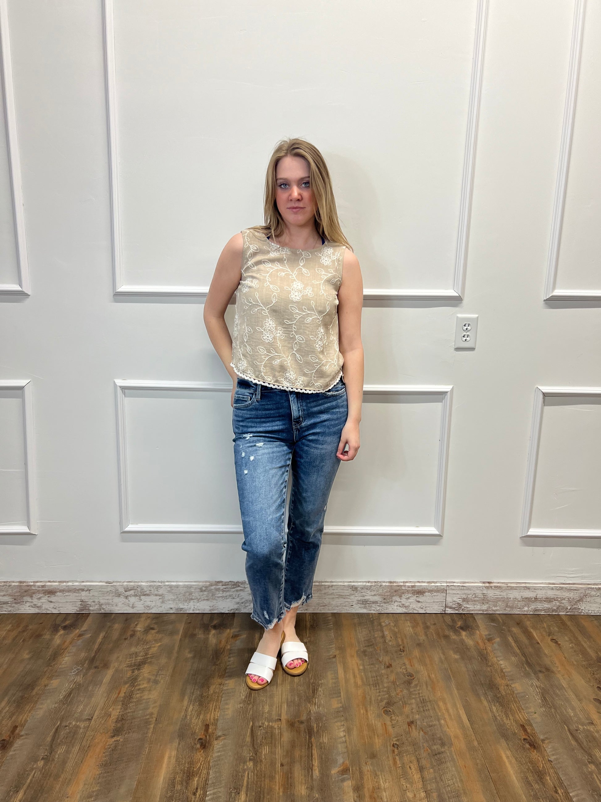 Person wearing a floral top and jeans standing in front of a white door.