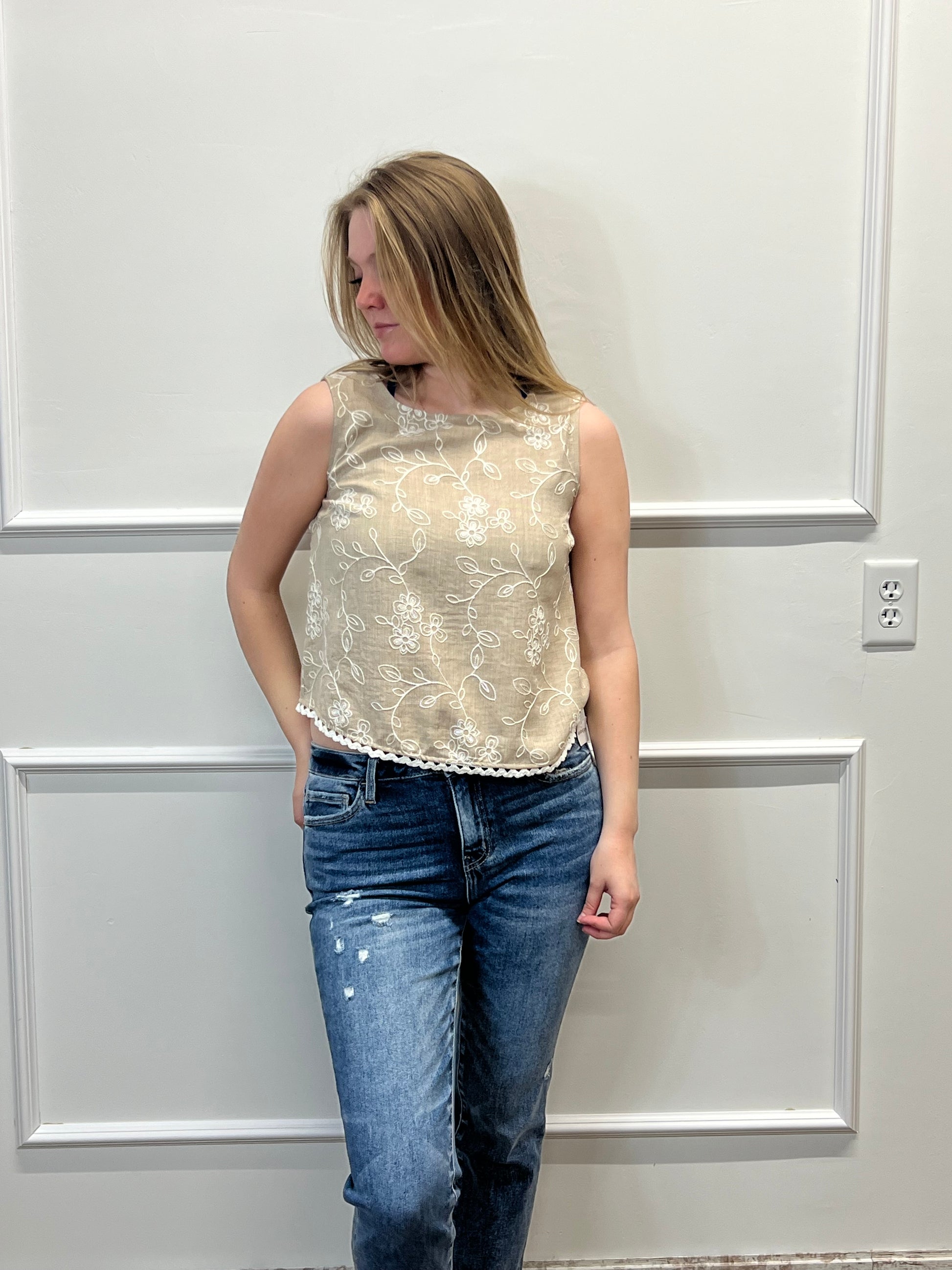 Person wearing a floral top and jeans standing against a white paneled wall.