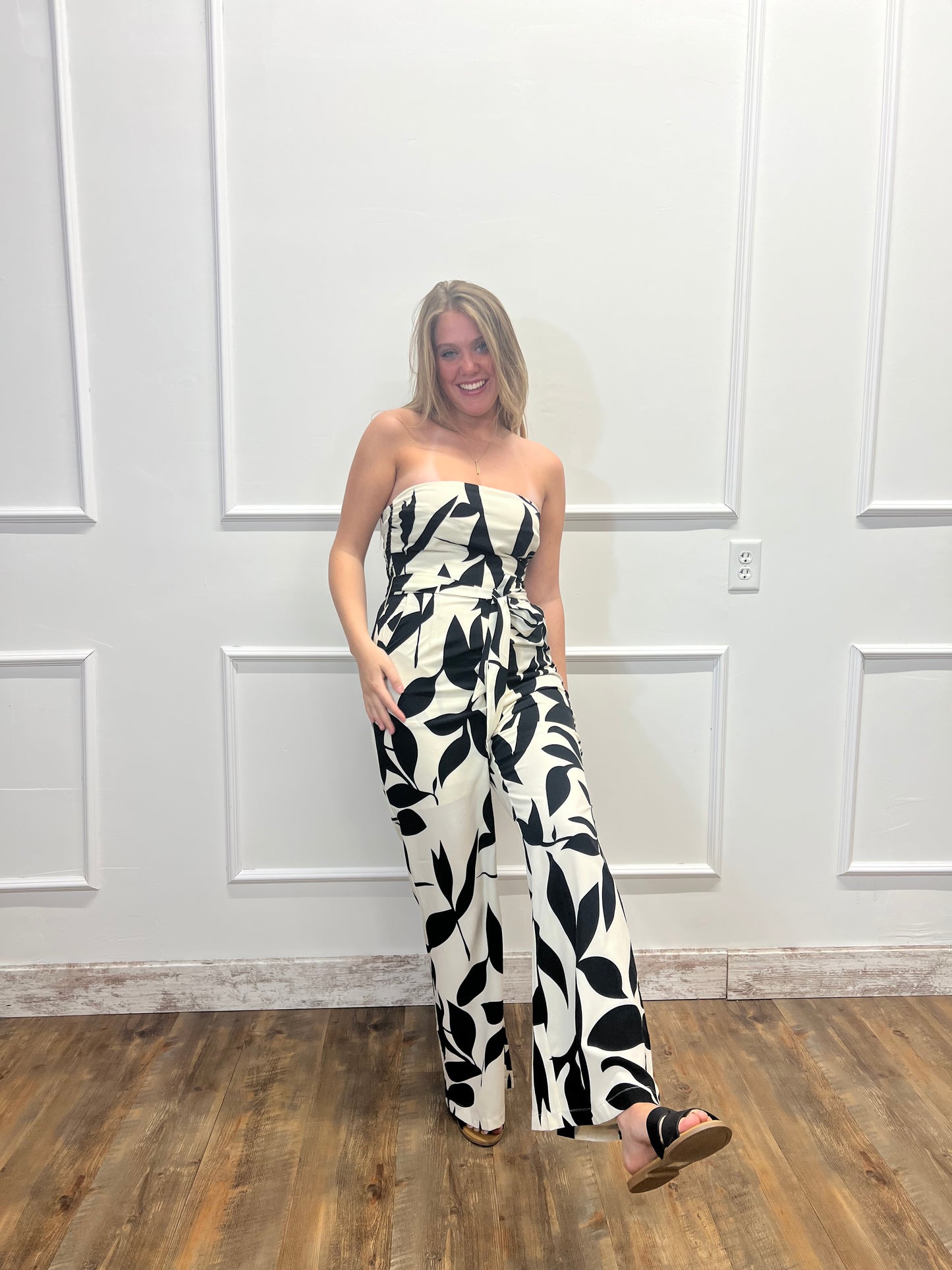 Person wearing a black and white patterned dress standing in front of a white paneled wall.