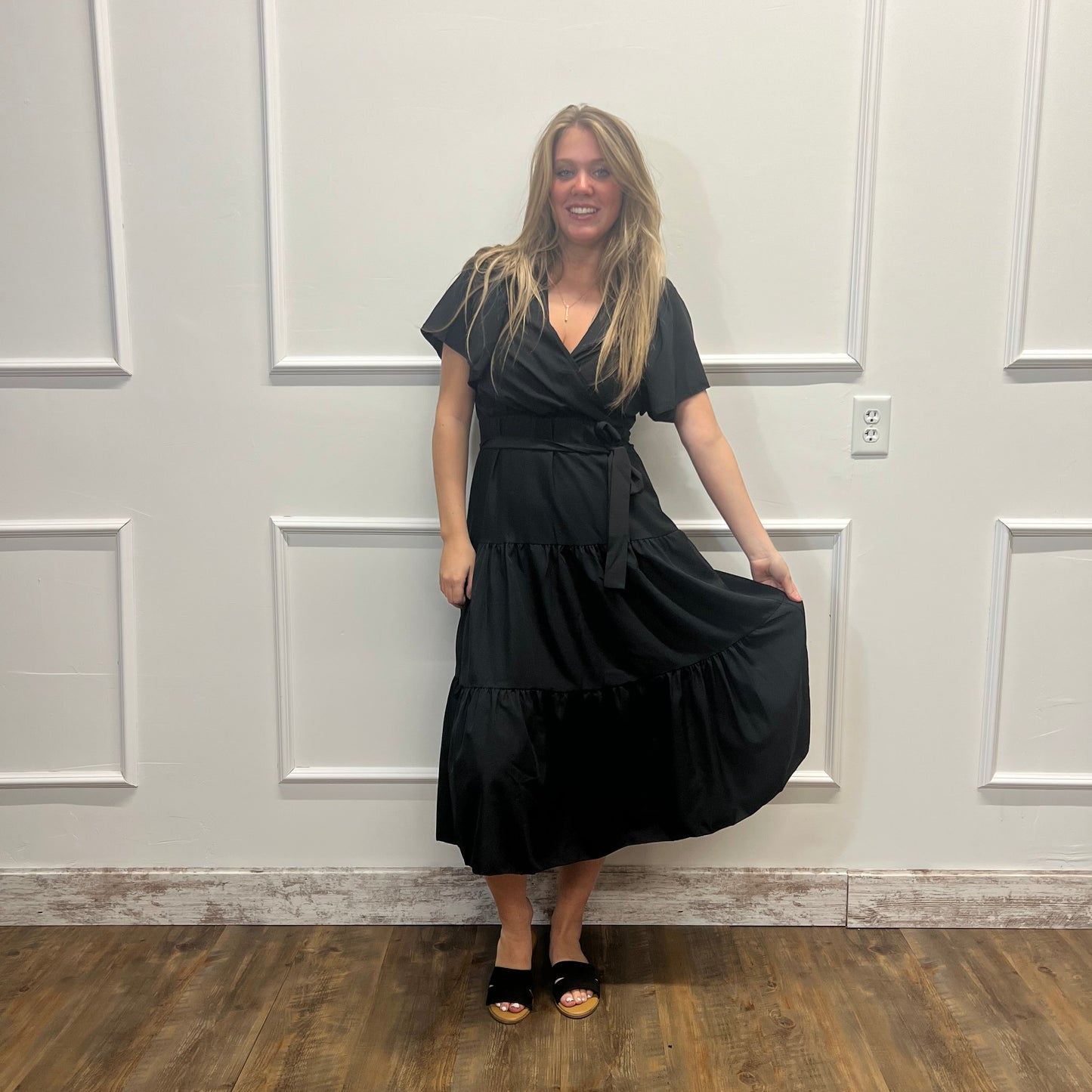 Person wearing a black outfit standing in a room with white walls and wooden flooring.