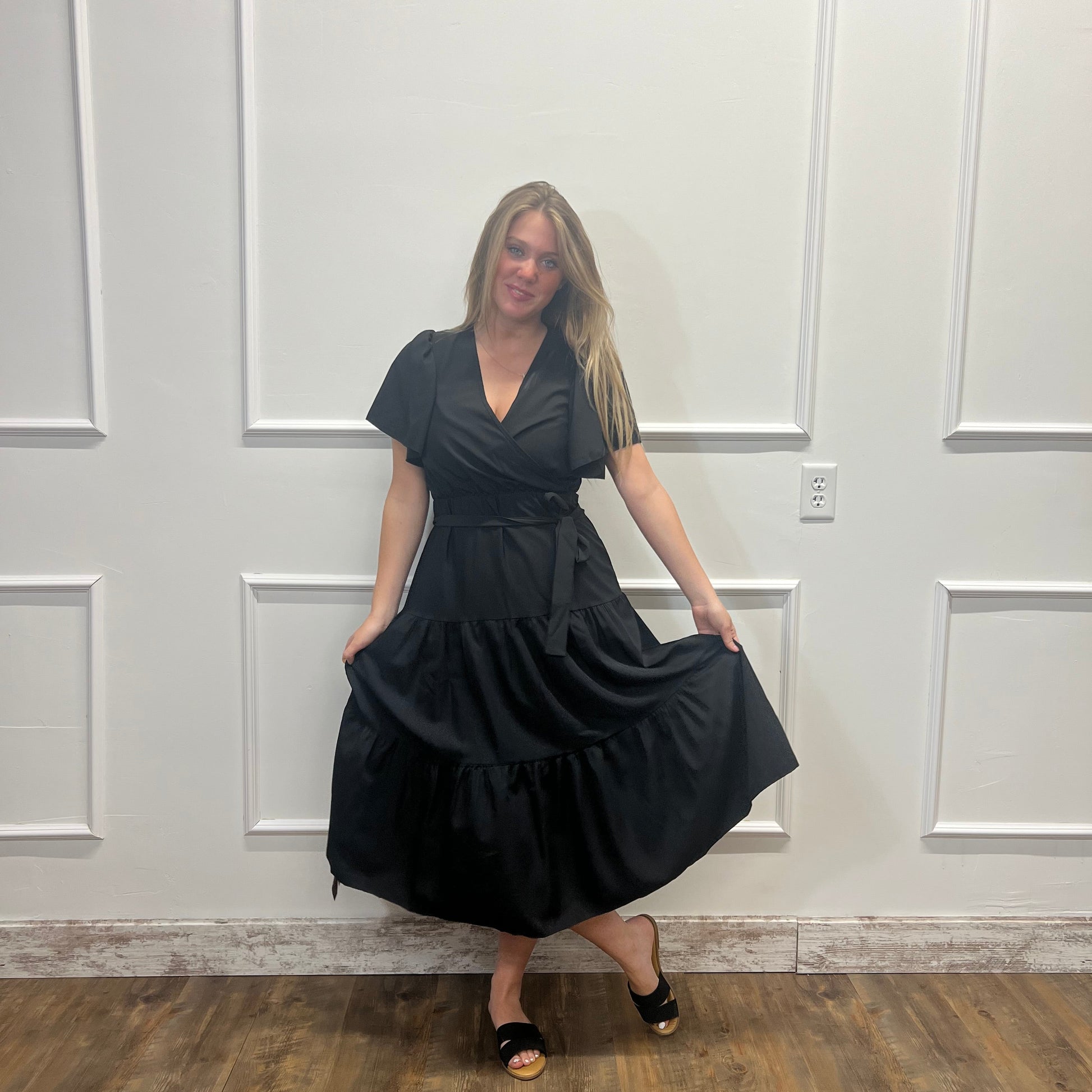 Person wearing a black dress standing in front of a white paneled door.