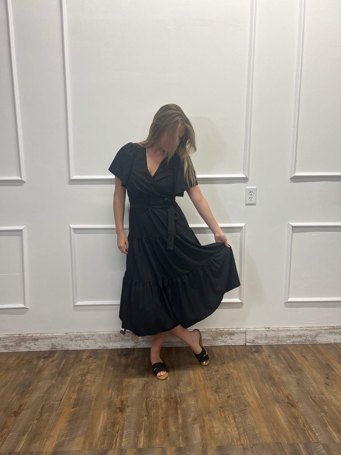 Person wearing a black dress standing in front of a white door with wooden floor.