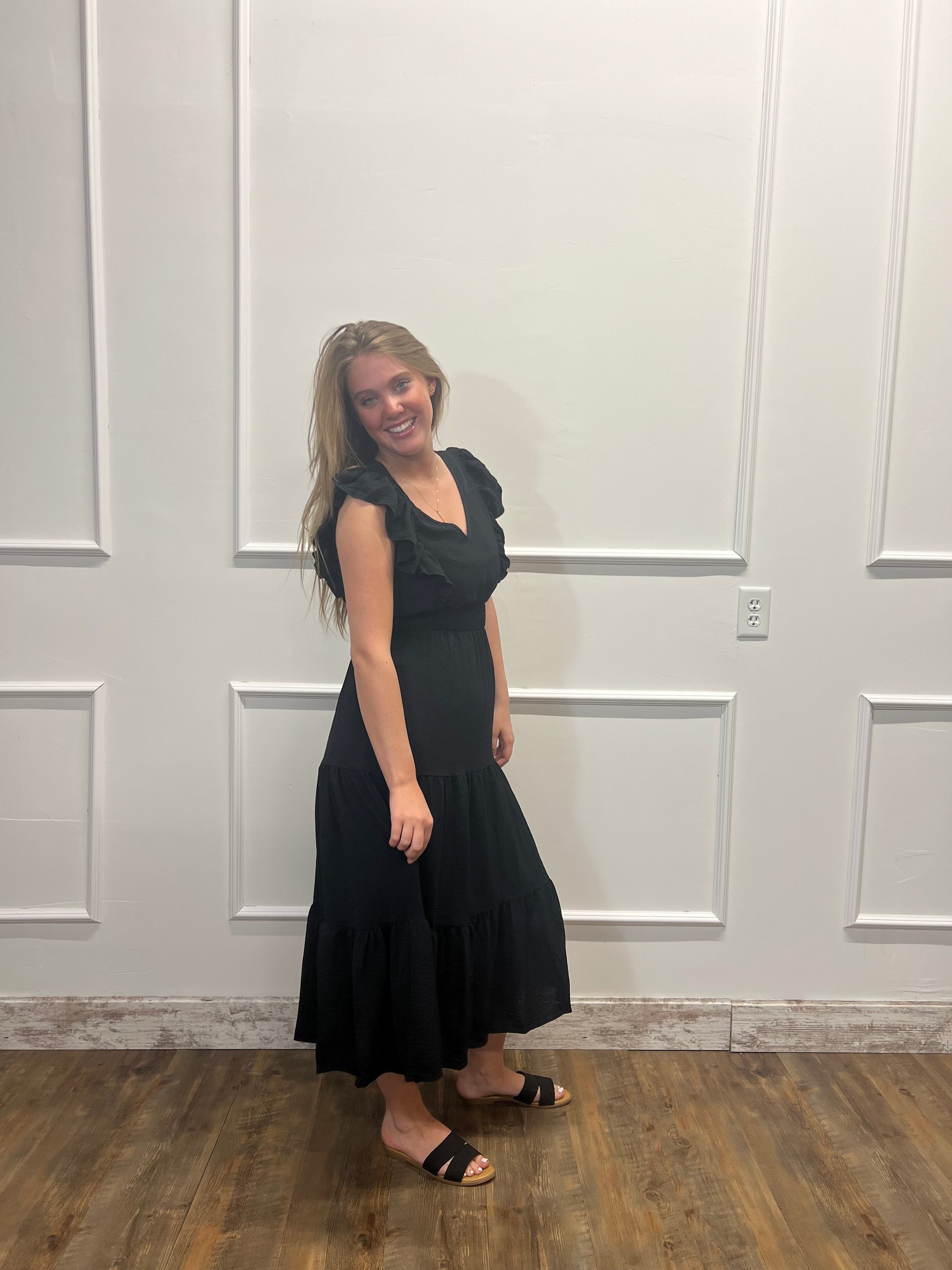 Woman wearing a black dress standing against a white paneled wall.