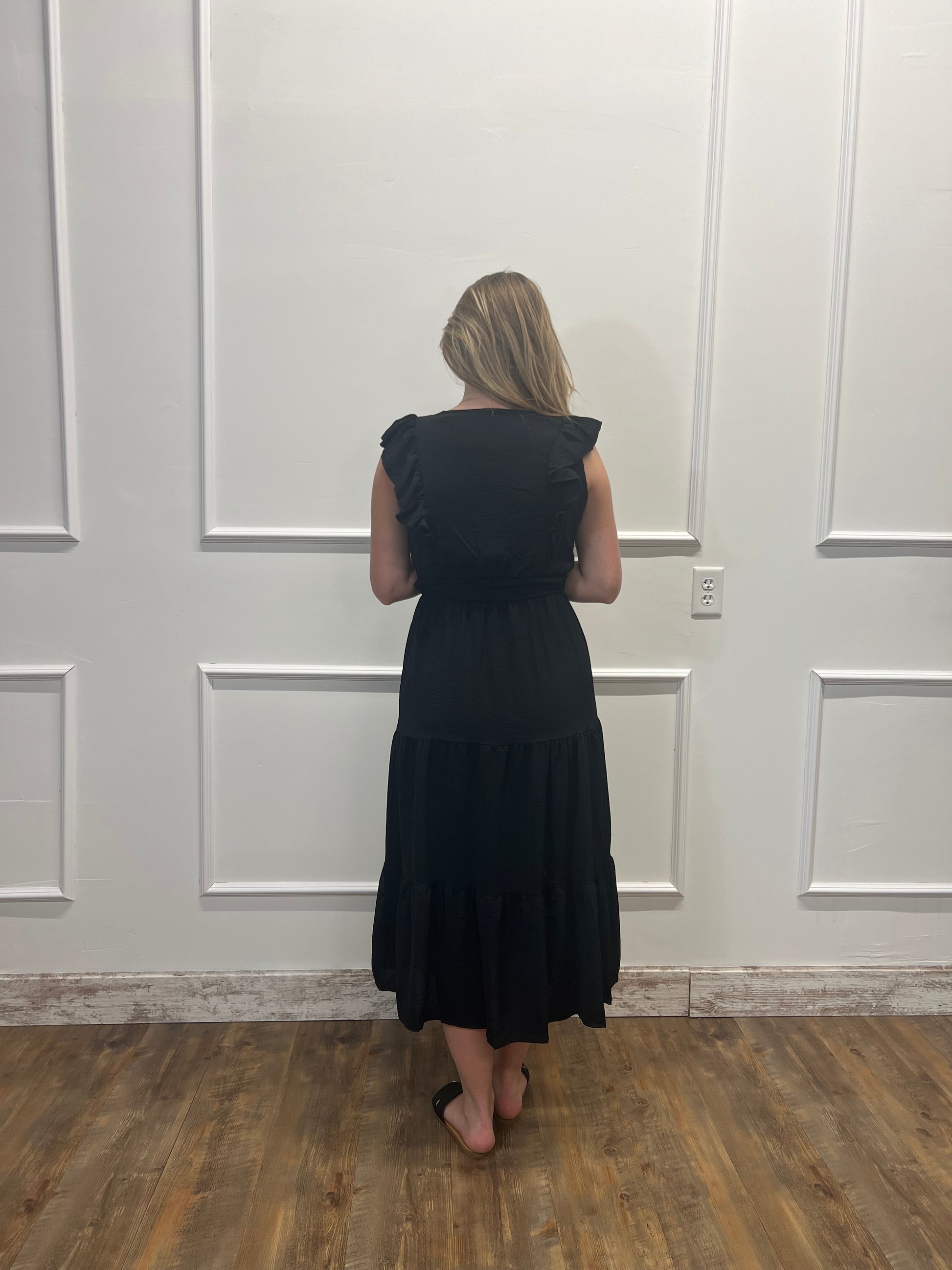 Person wearing a black dress standing in front of a white door.