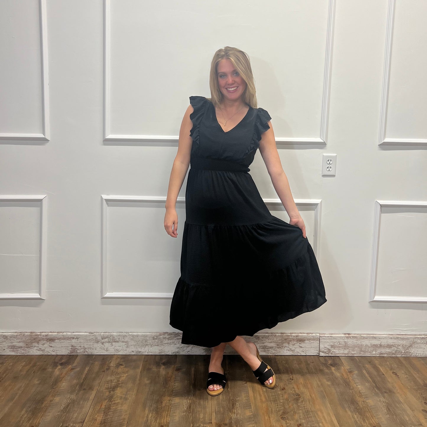 Person wearing a black dress standing in front of a white door.