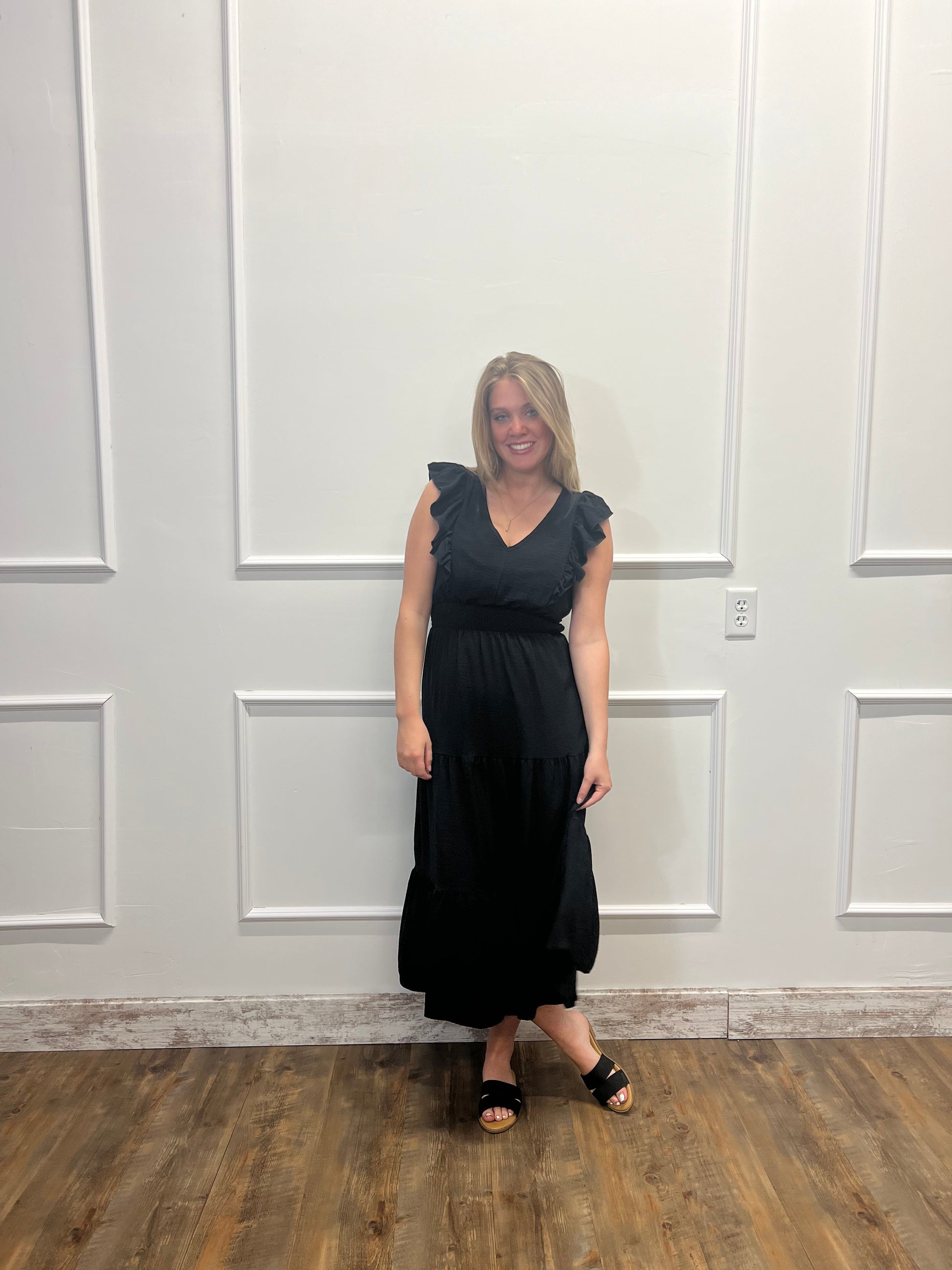 Person wearing a black dress standing in front of a white door with wooden floor.