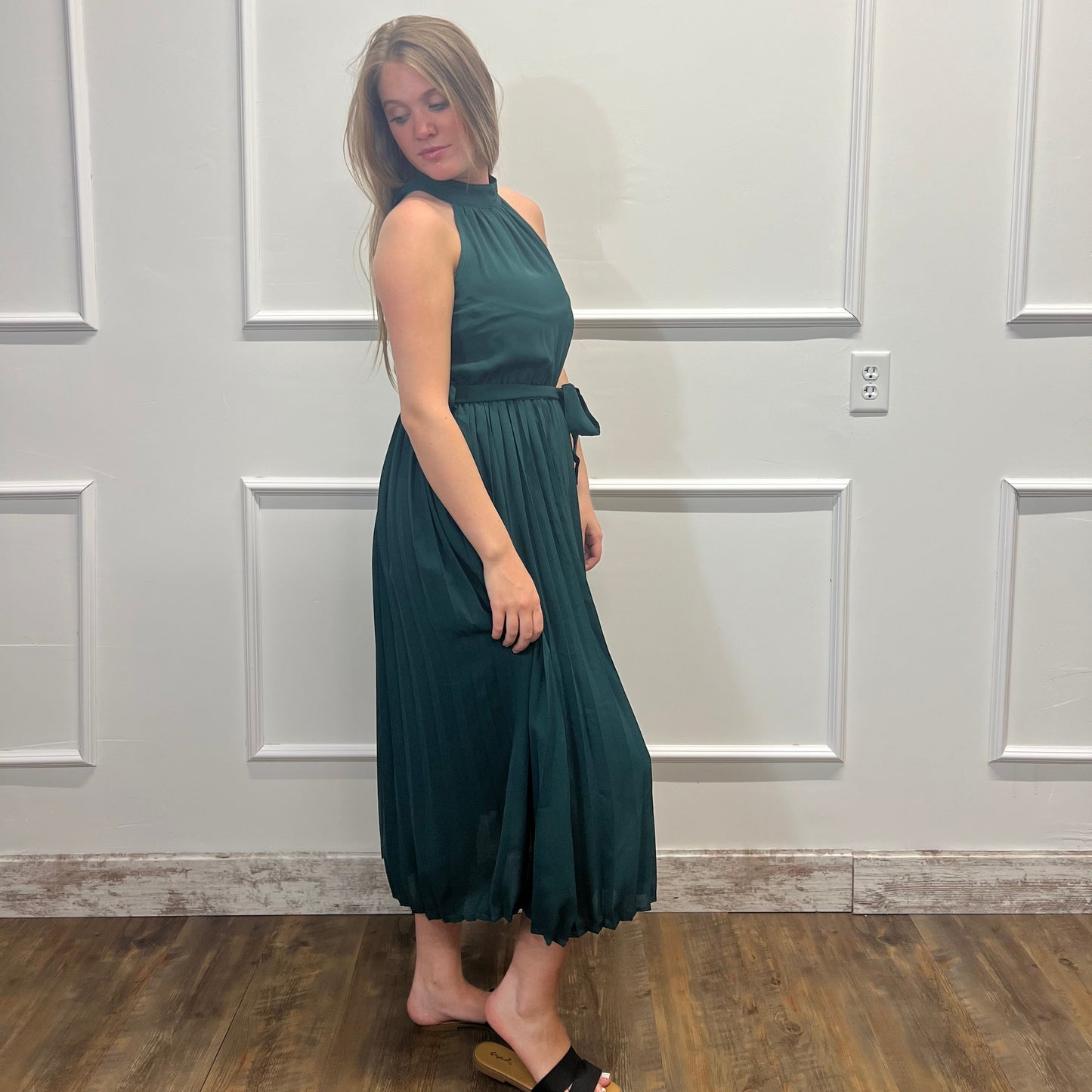 Woman wearing a green dress standing against a white paneled wall.