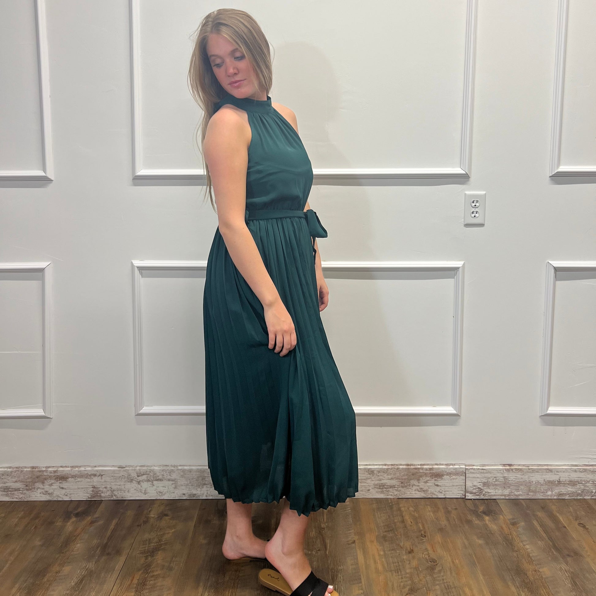 Woman wearing a green dress standing against a white paneled wall.