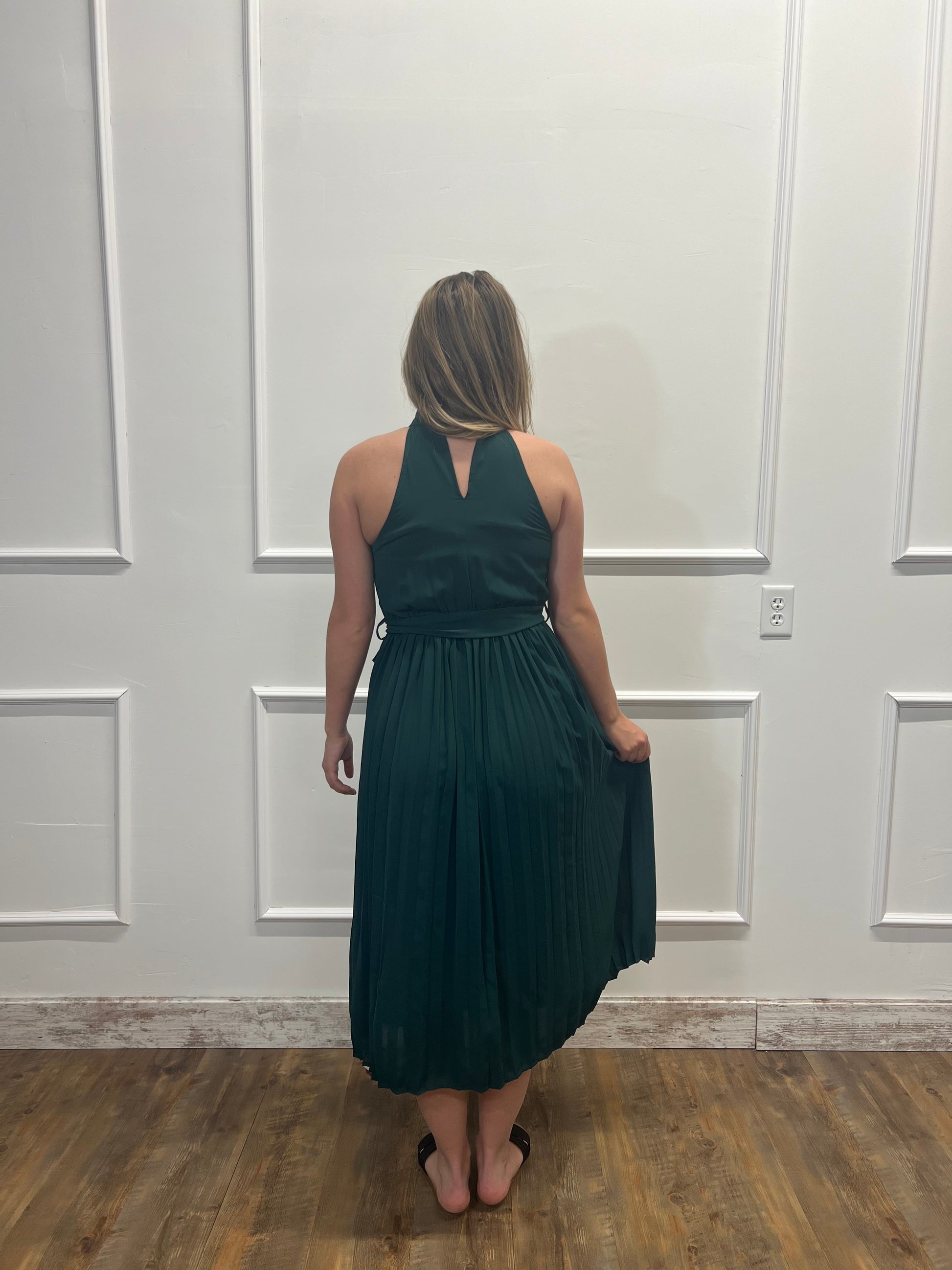 Woman wearing a dark green dress standing in front of a white paneled wall.