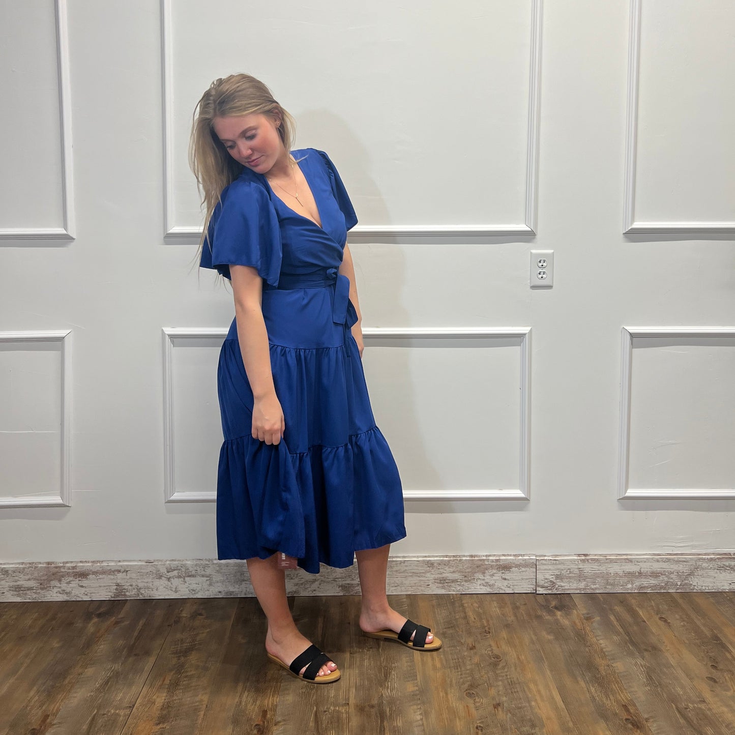 Woman in a blue dress standing in front of a white door.