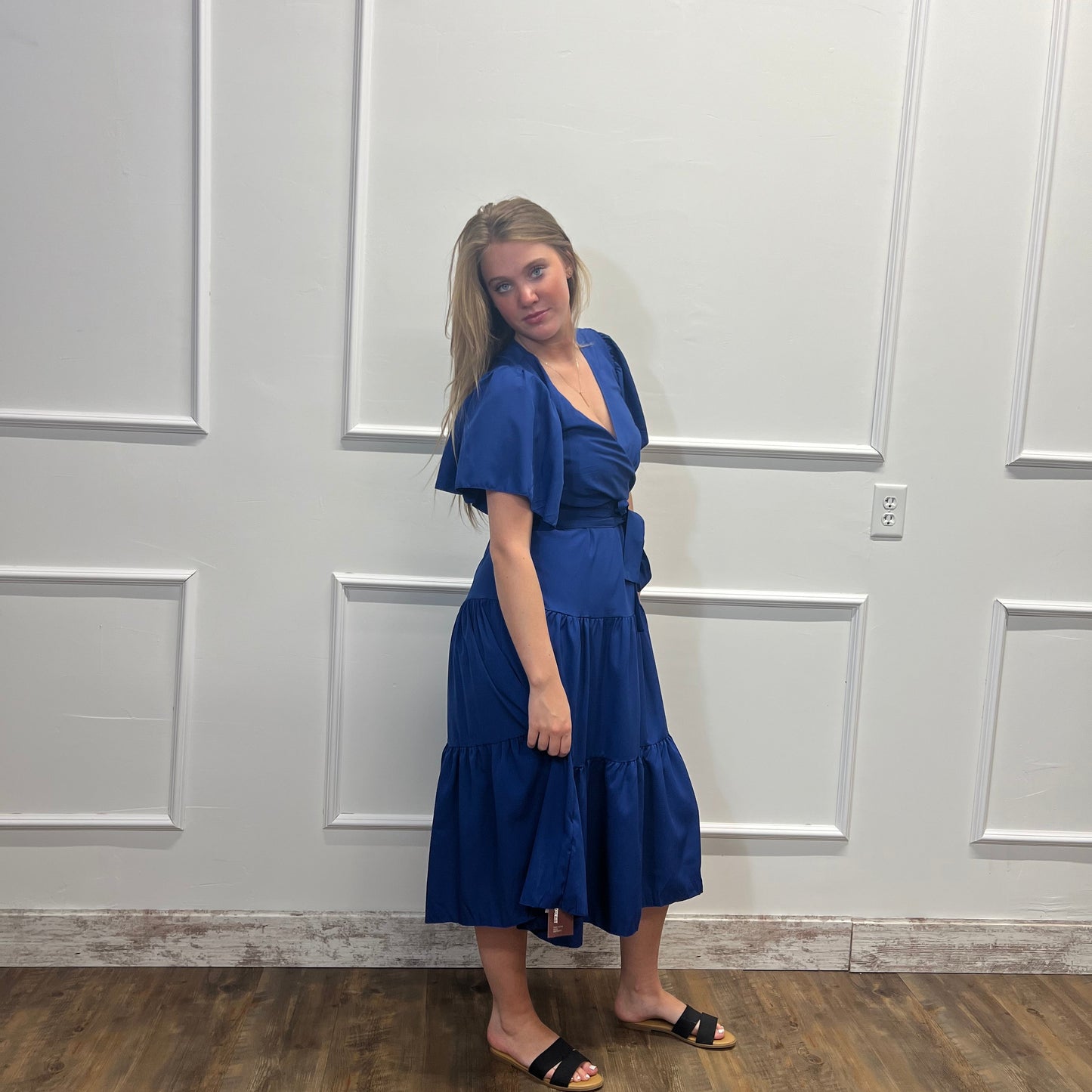 Woman in a blue dress standing in front of a white door.