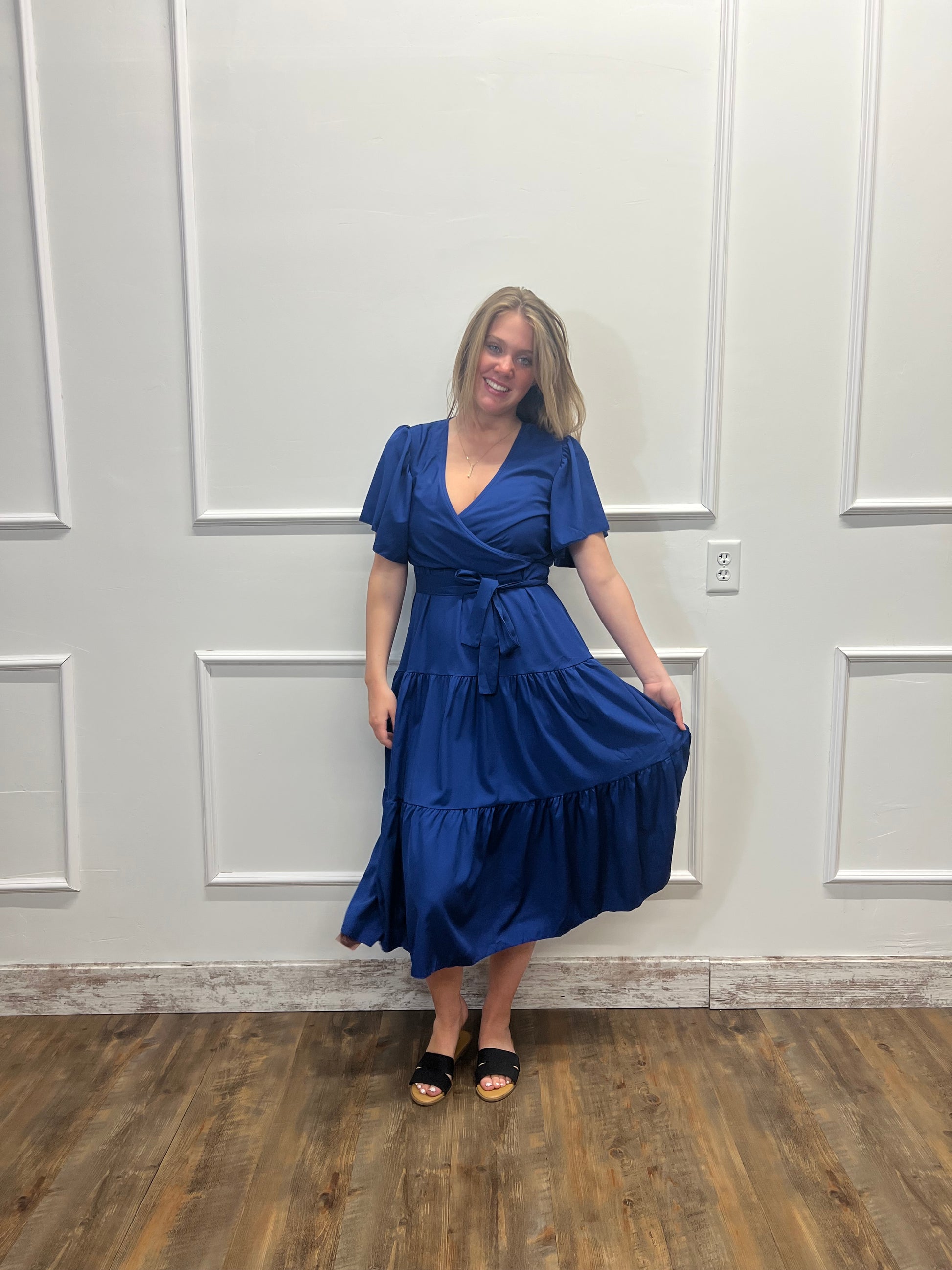 Woman in a blue dress standing in front of a white paneled wall.