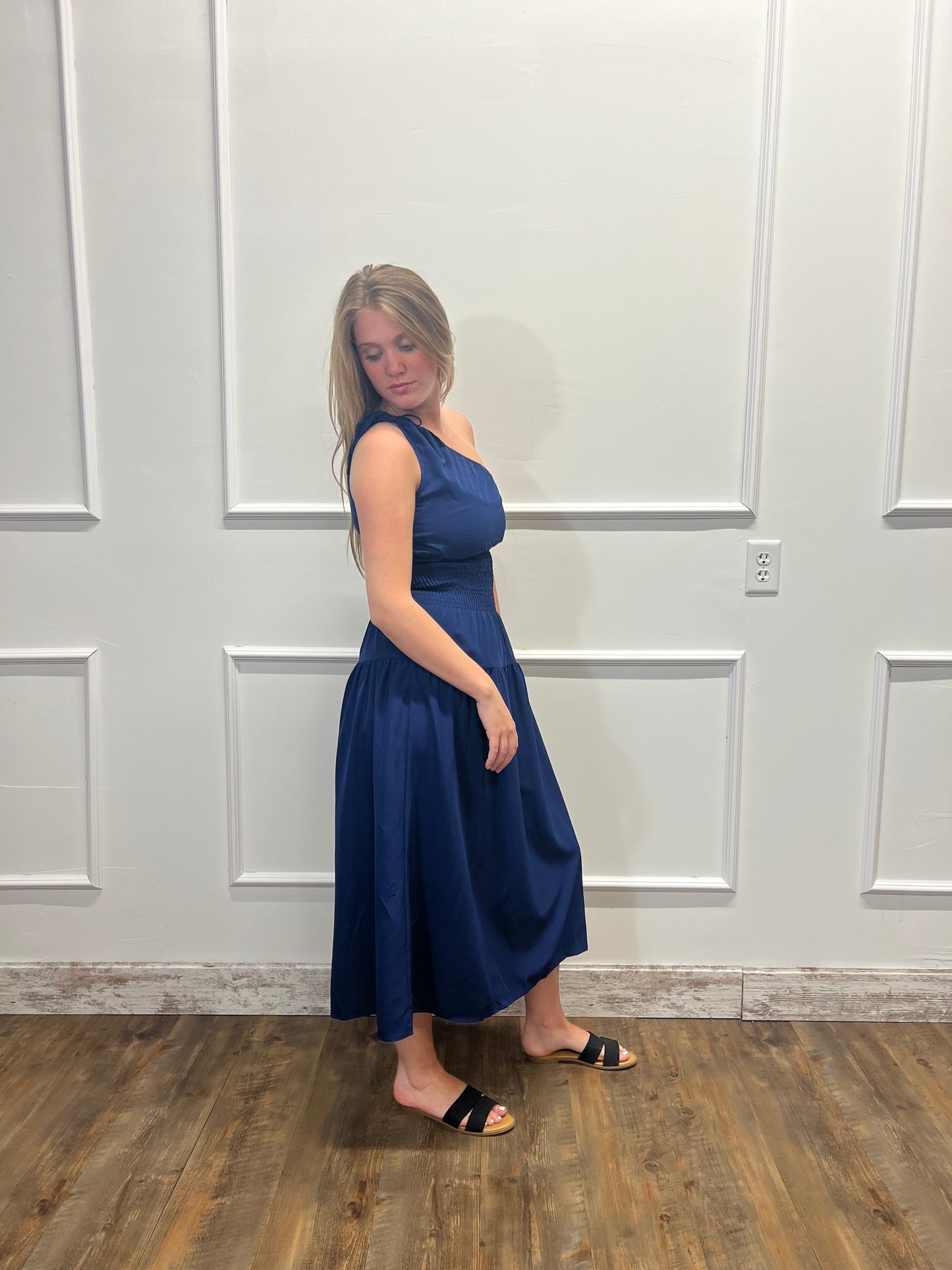 Woman in a blue dress standing against a white paneled wall.