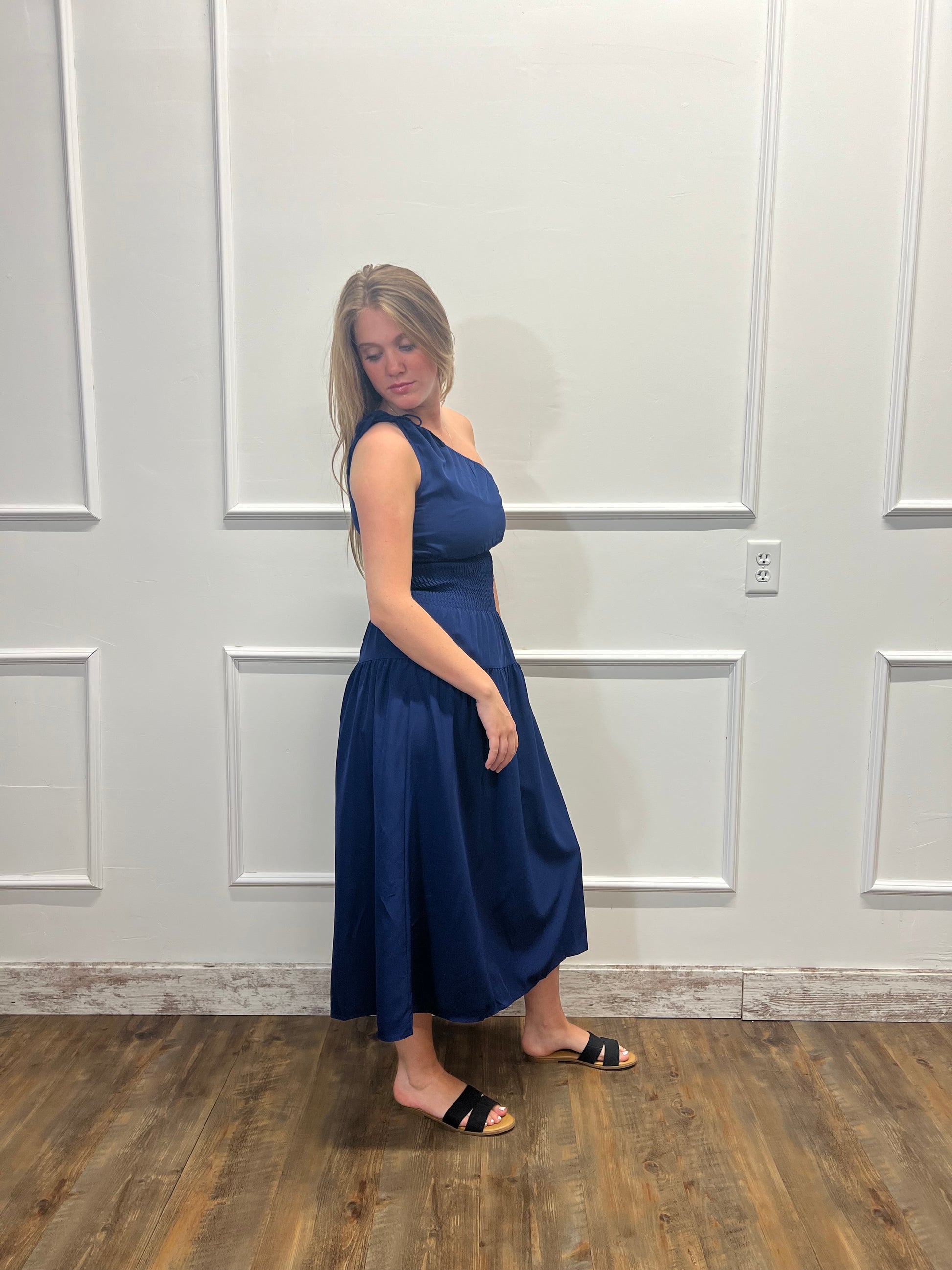 Woman in a blue dress standing against a white paneled wall.