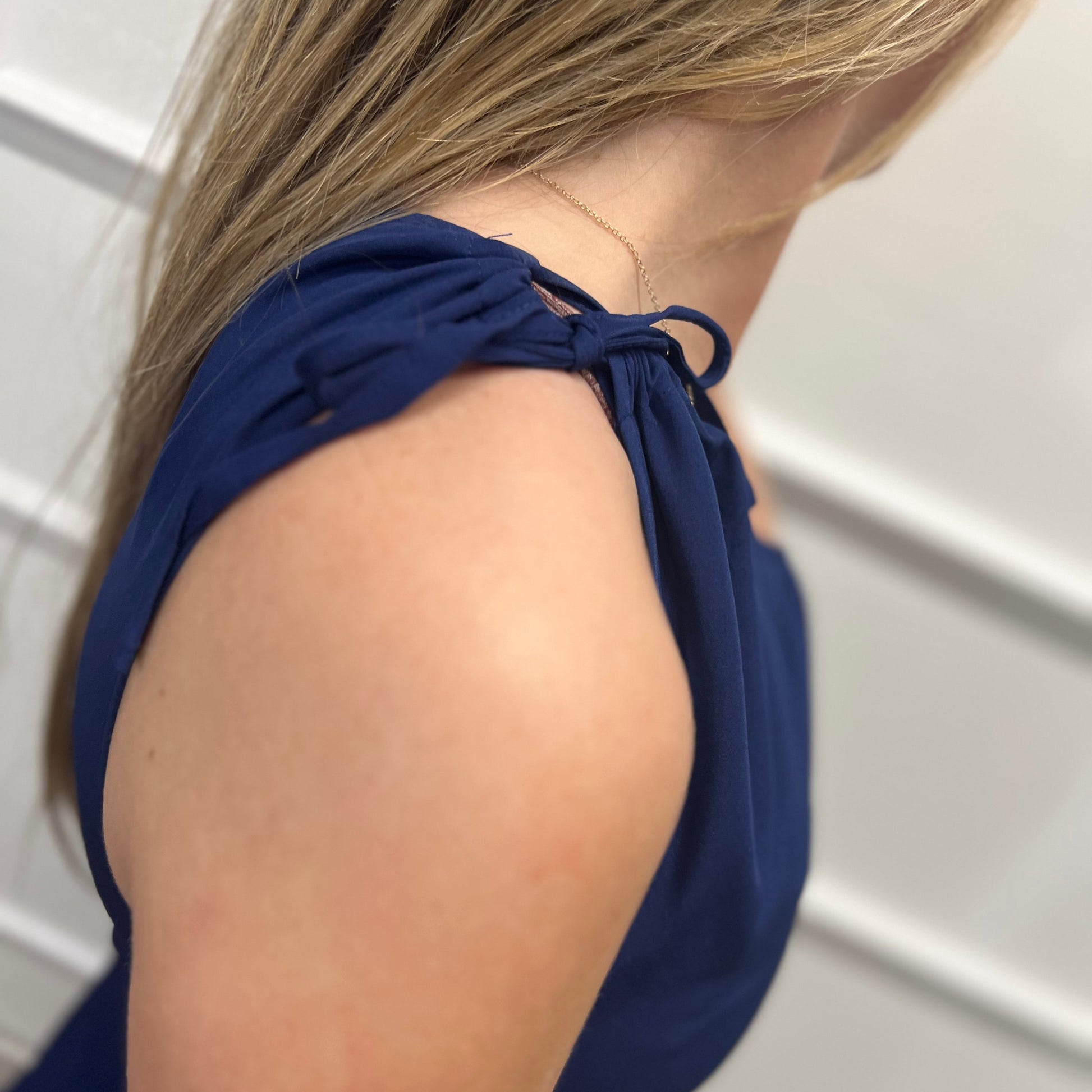 Navy blue halter top worn by a person against a white tiled wall.