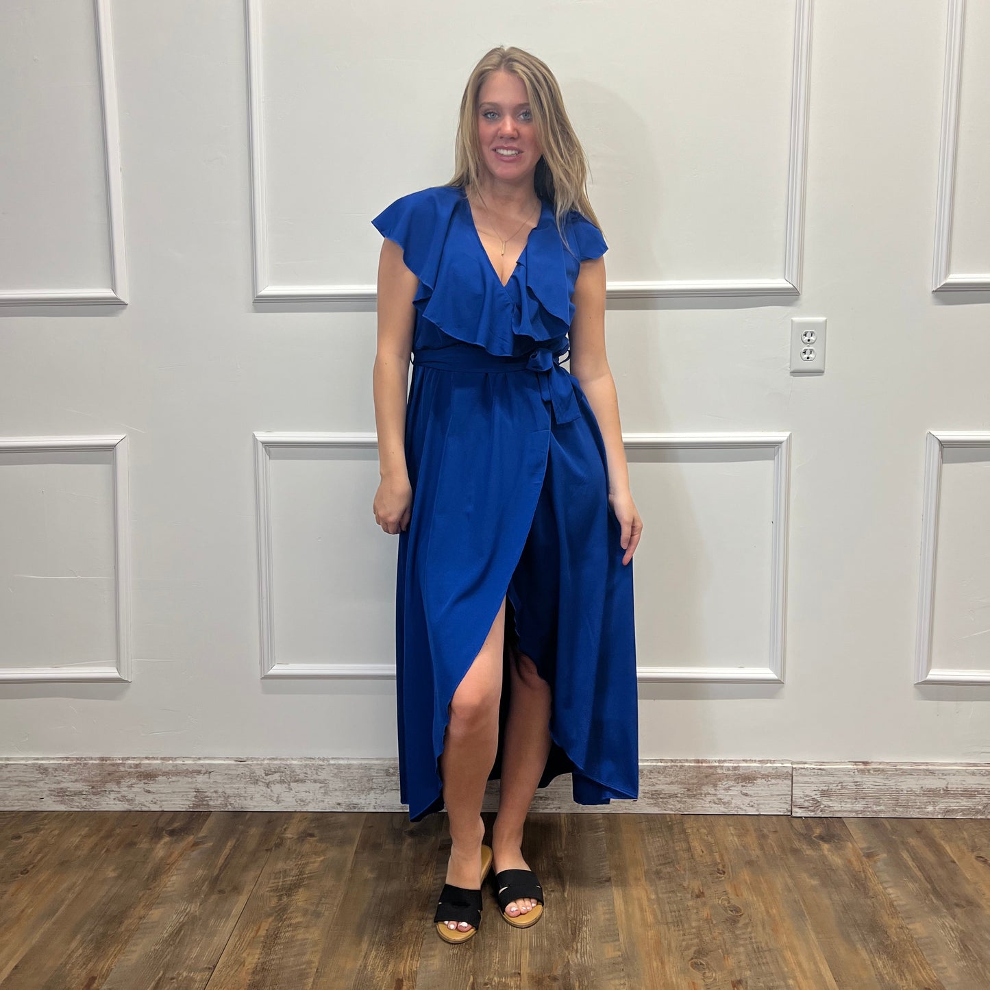 Woman in a blue dress standing in a room with white walls and wooden flooring.