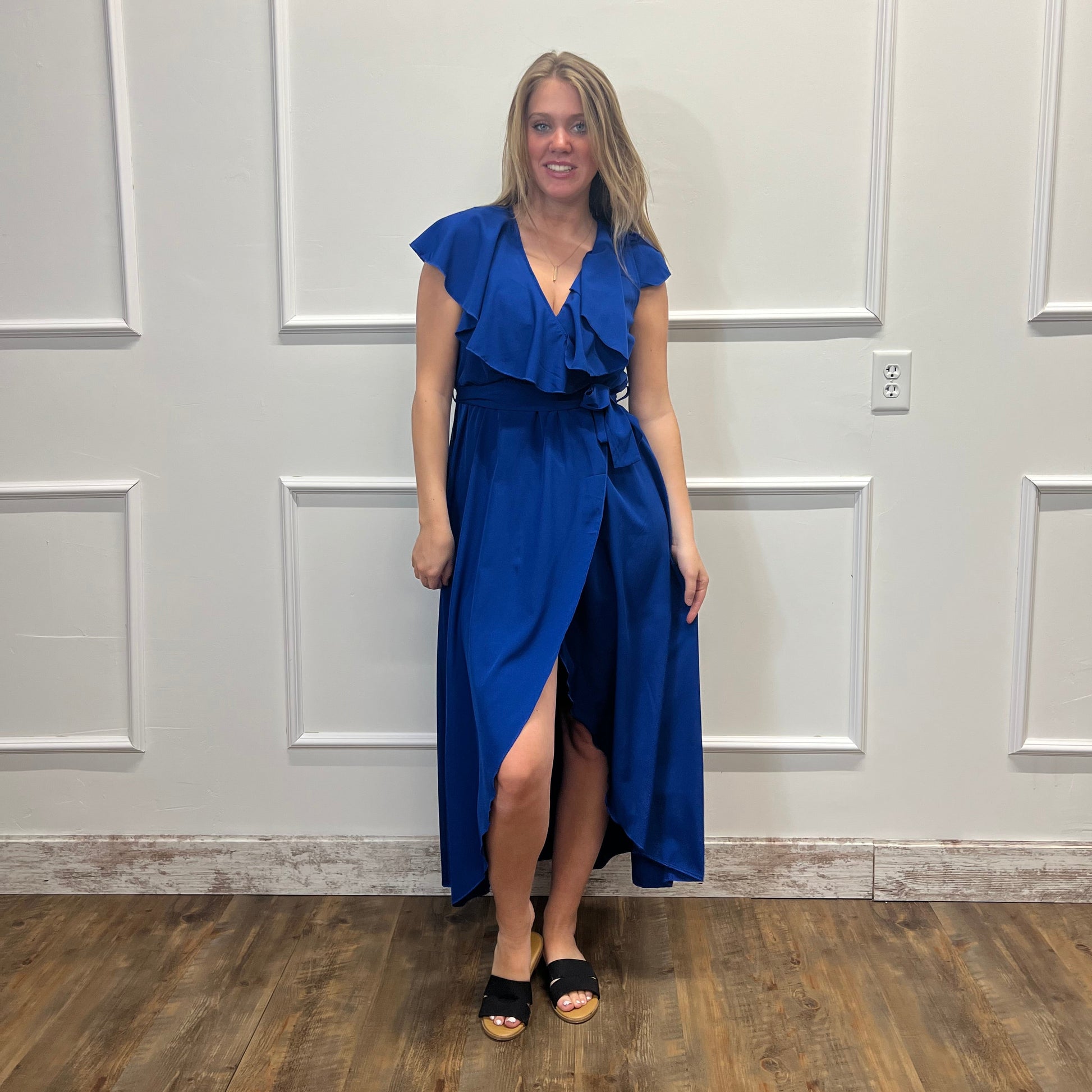Woman in a blue dress standing in a room with white walls and wooden flooring.