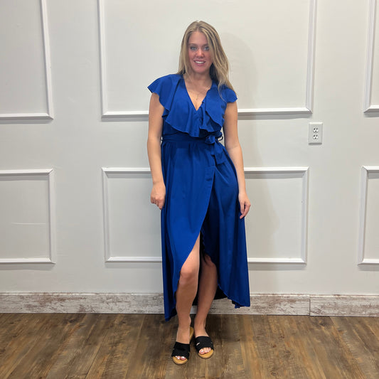 Woman in a blue dress standing in a room with wooden flooring and white walls.