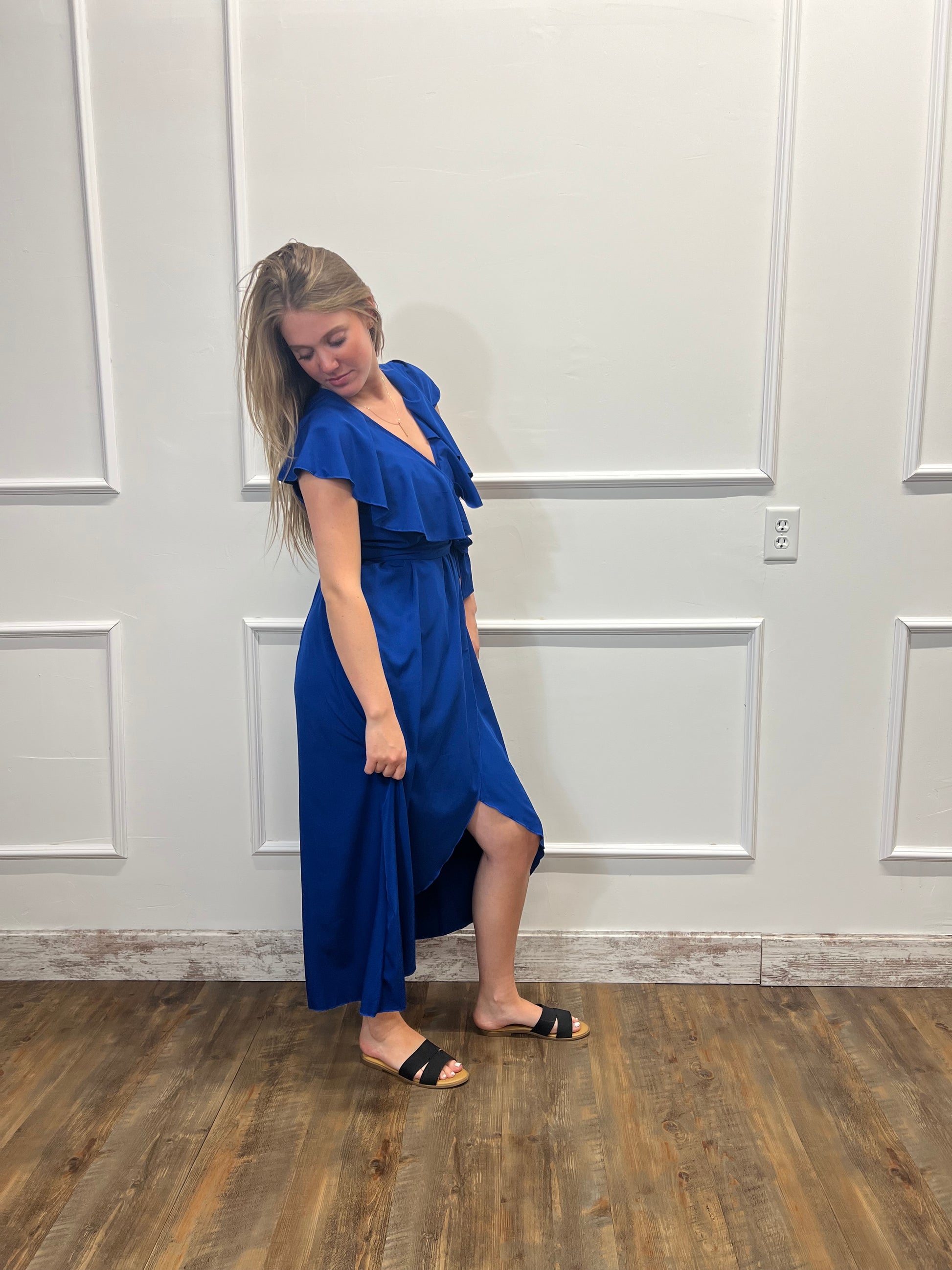 Woman in a blue dress lying on a wooden floor against a white paneled wall.