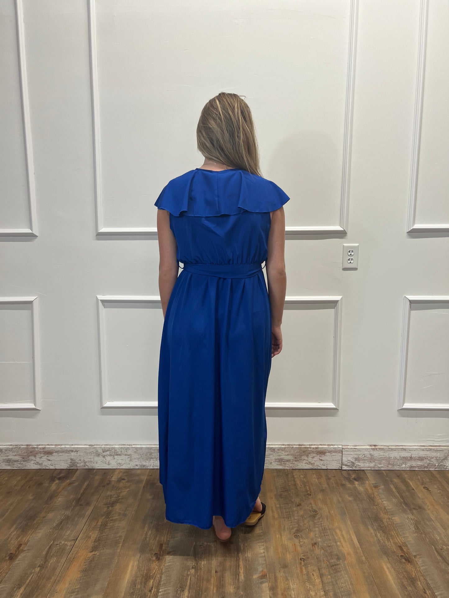 Person wearing a blue dress standing in front of a white door.