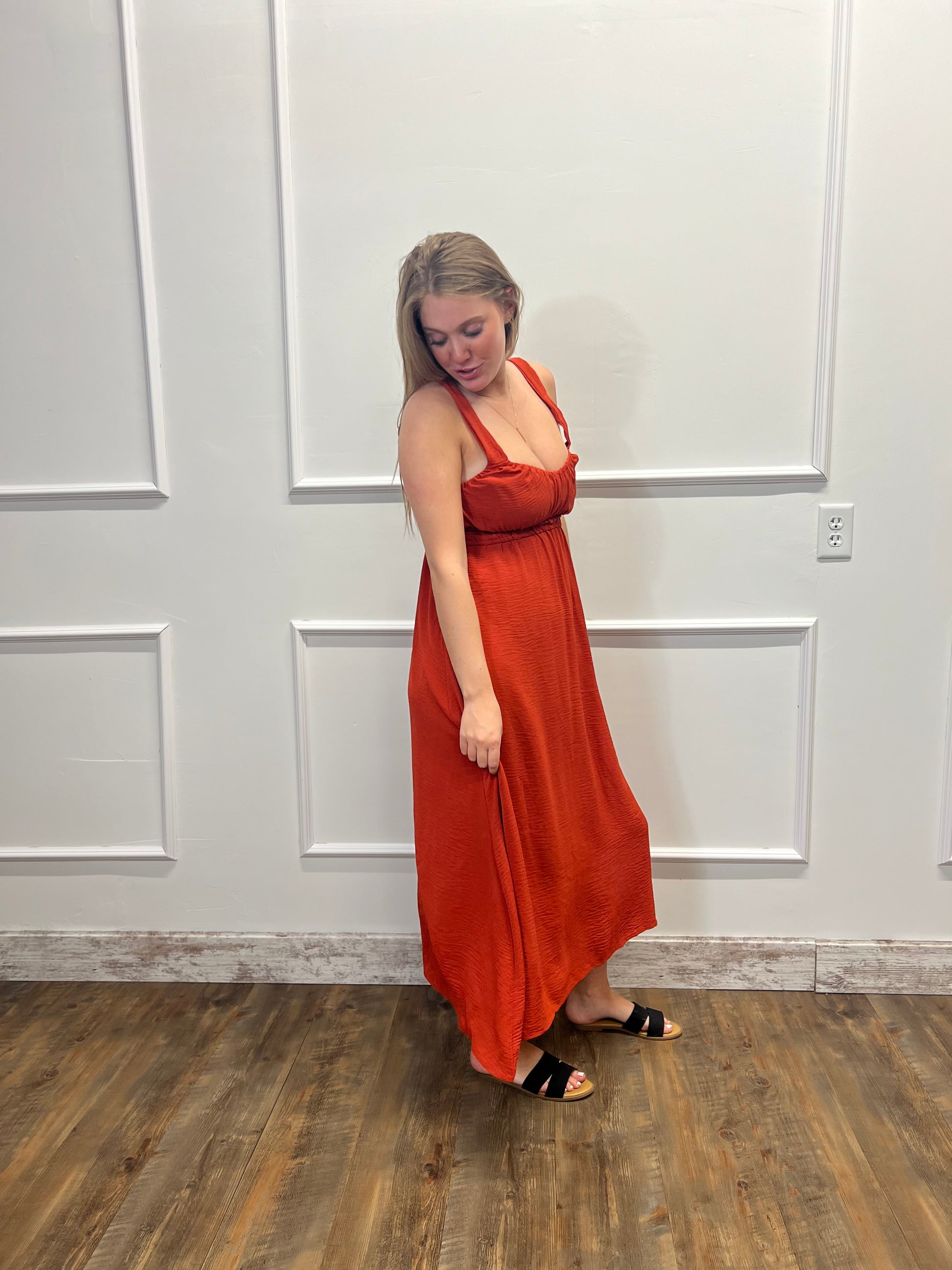 Woman wearing a rust-colored dress standing against a white paneled wall.