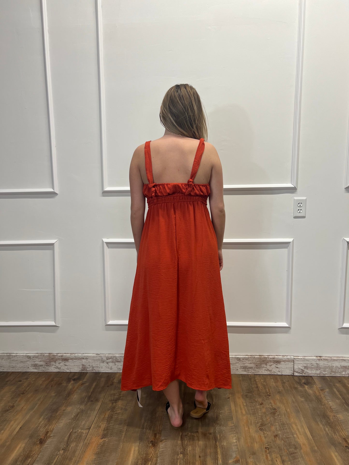 Person wearing an orange dress standing in a room with white paneled walls and wooden flooring.