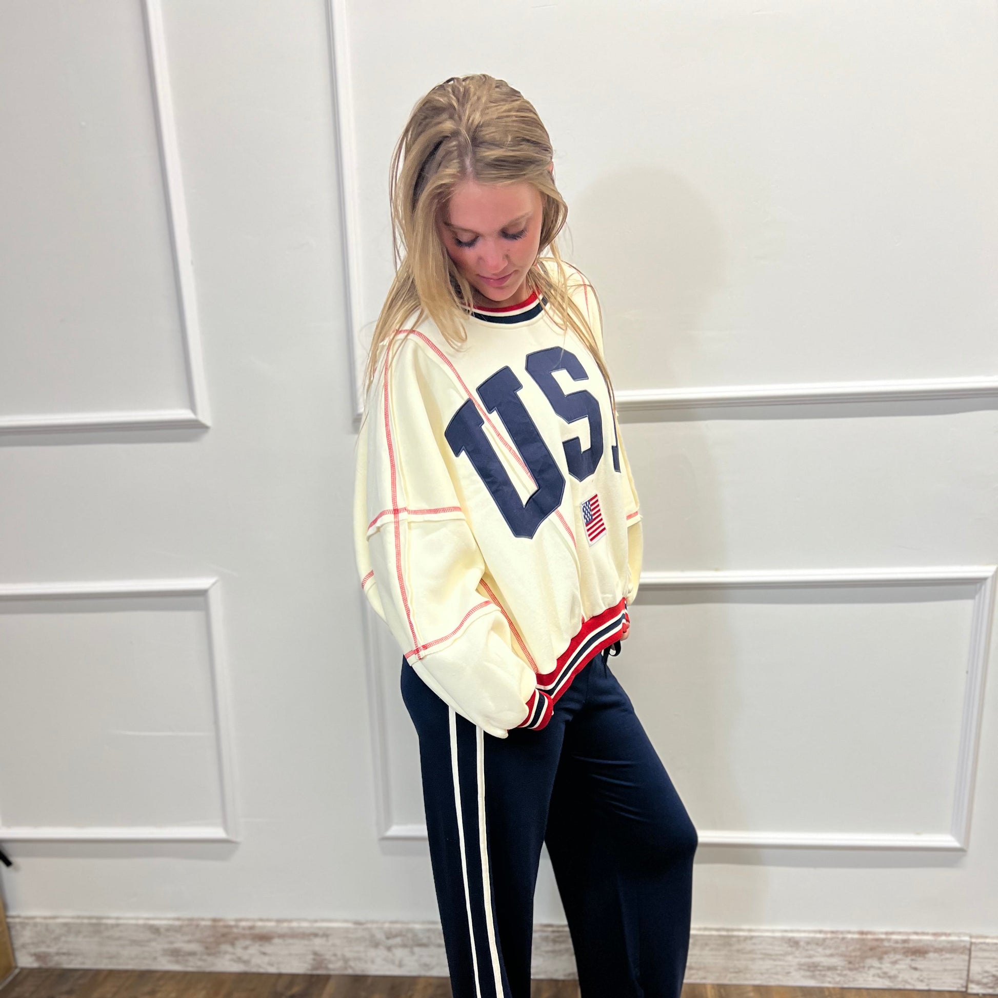 Person wearing a 'USA' sweatshirt and navy pants with white stripes indoors.