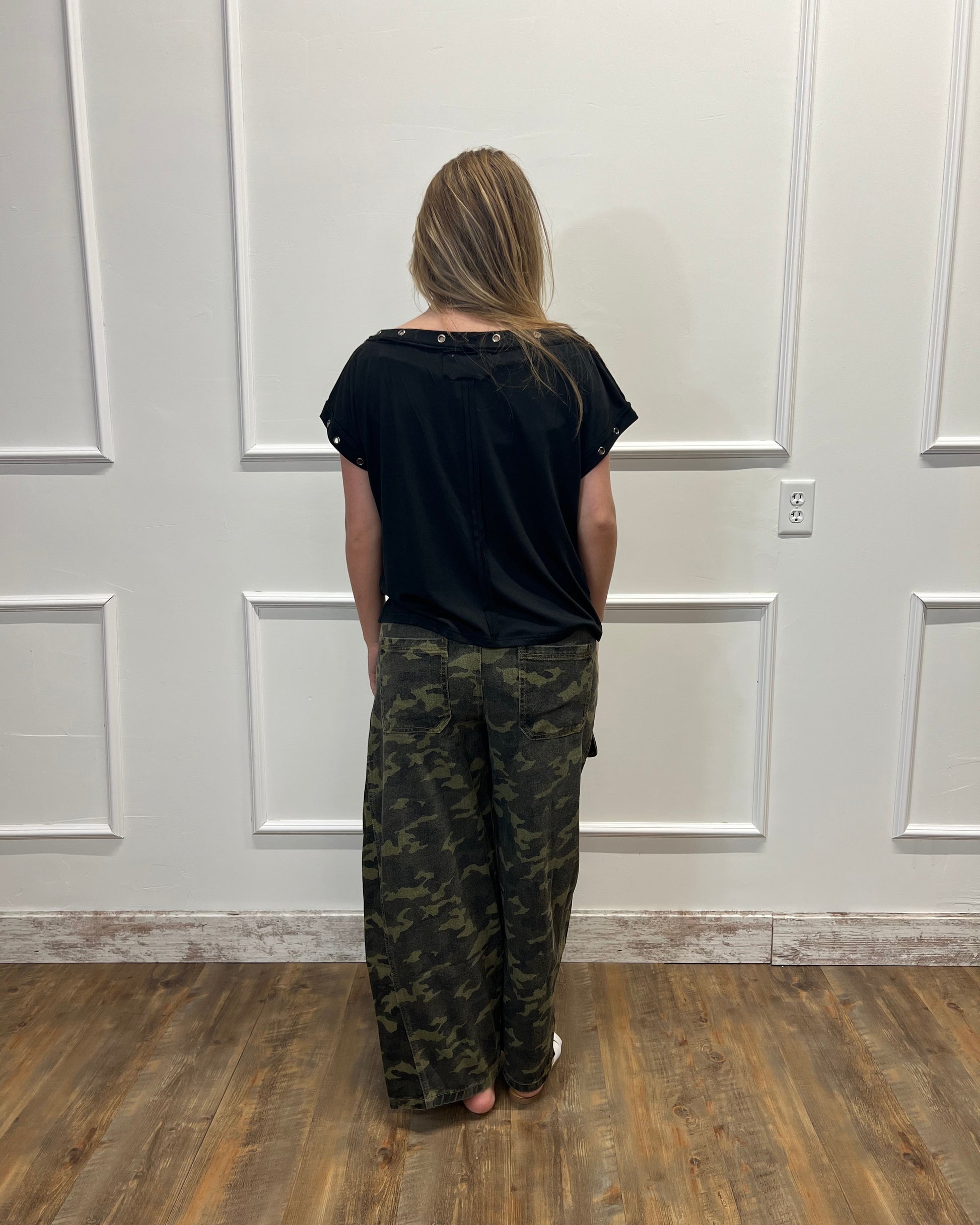Person wearing a black shirt and camouflage pants standing in front of a white door.