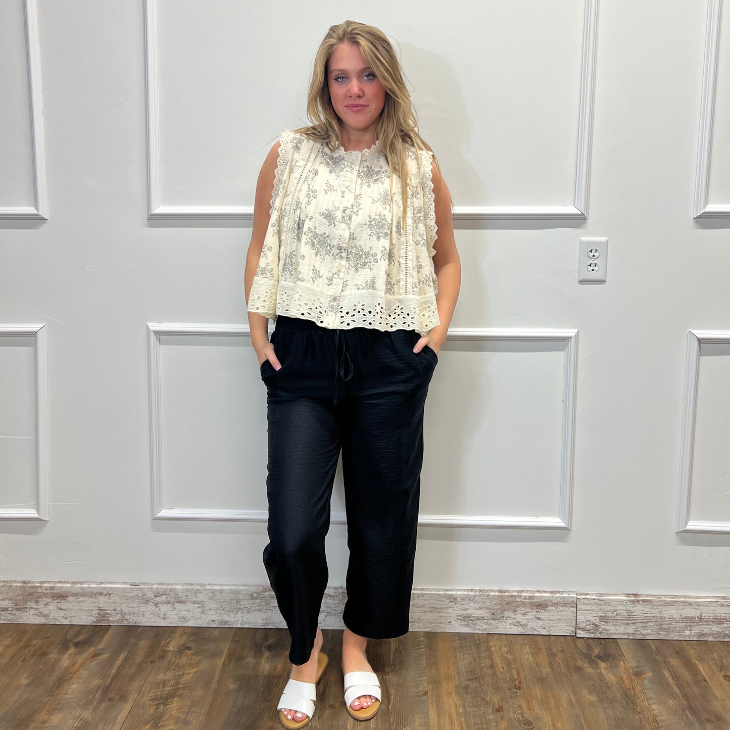 Person wearing a white lace top and black pants standing in front of a white door.