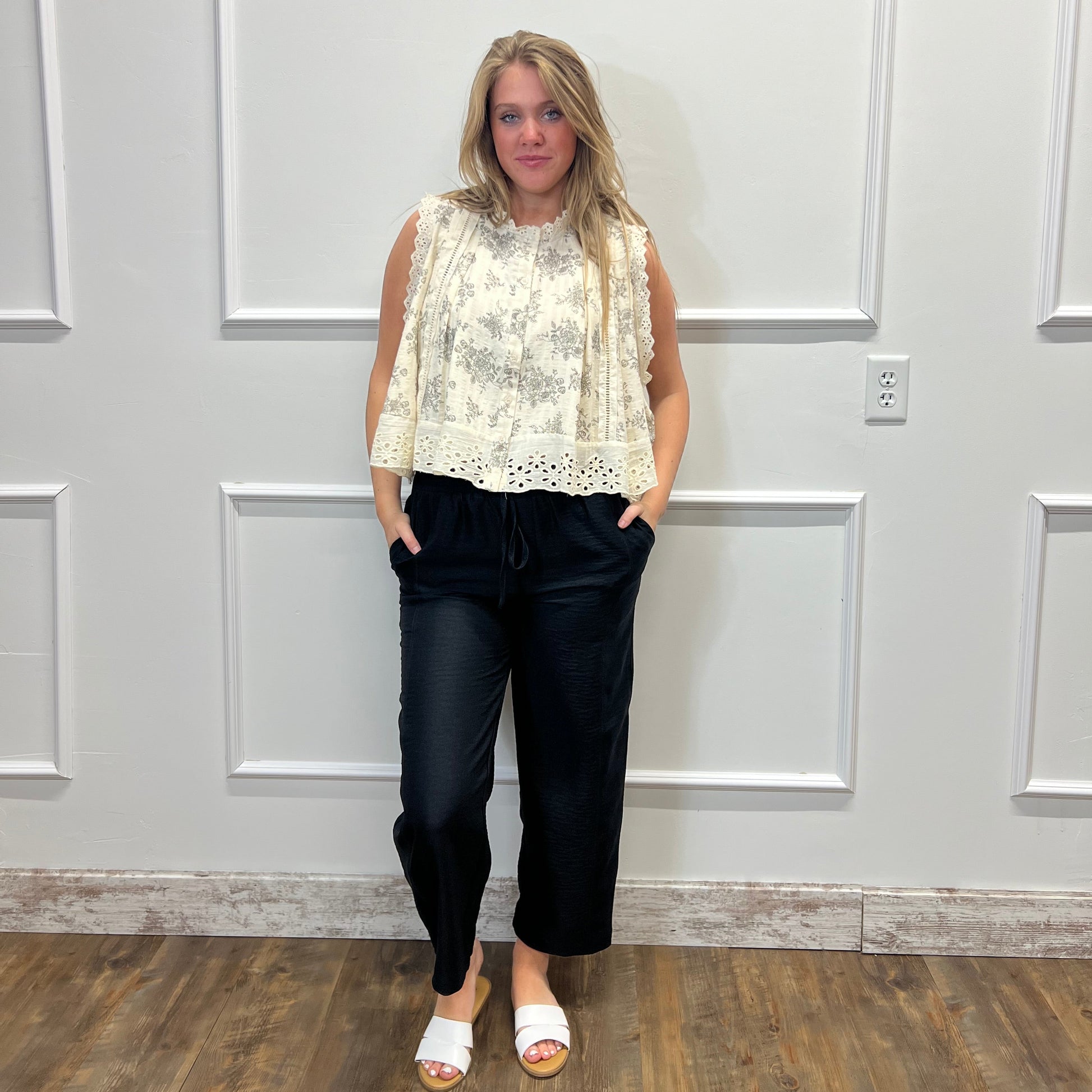 Person wearing a white lace top and black pants standing in front of a white door.